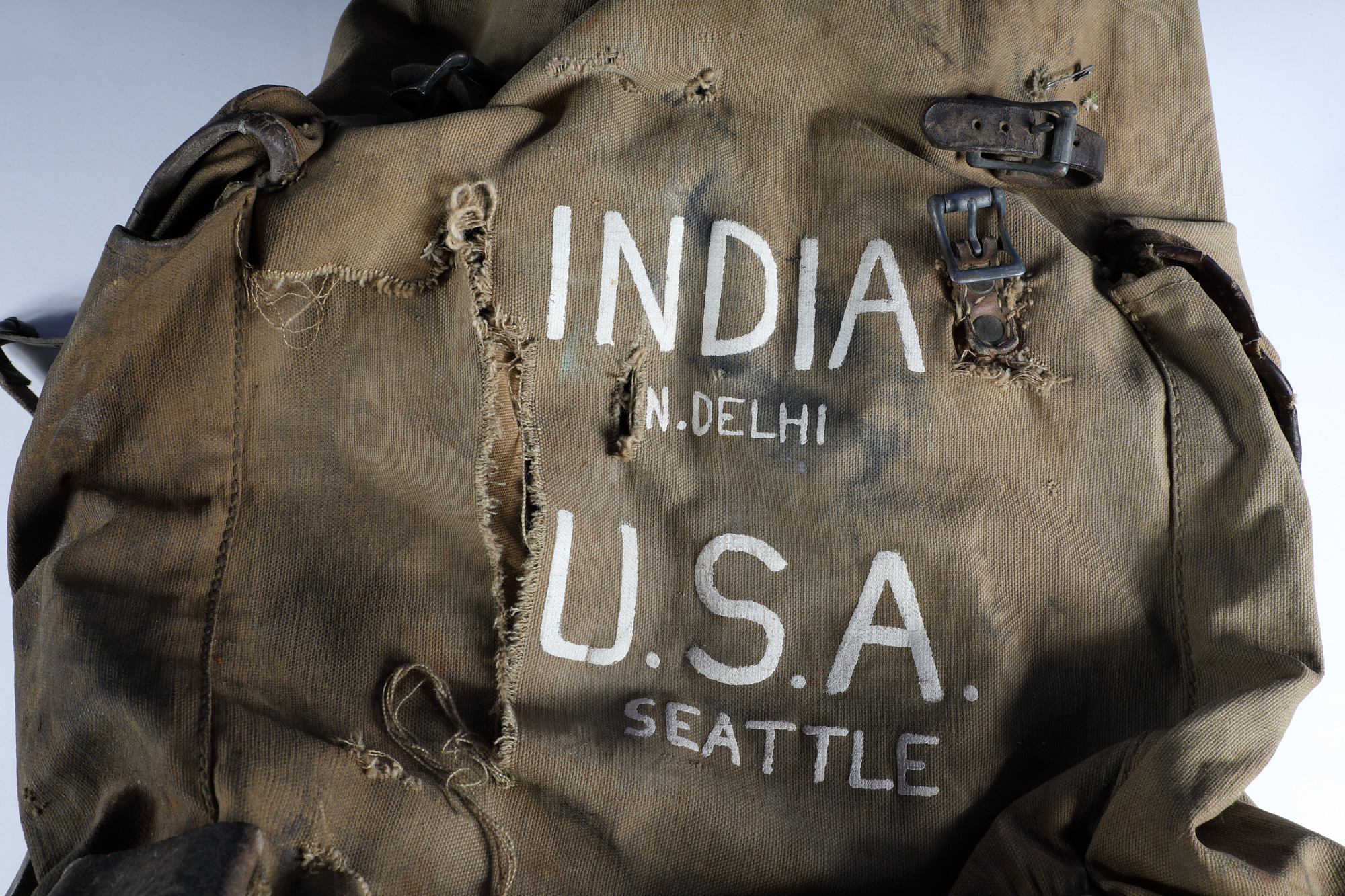 A worn, torn backpack with INDIA NEW DELHI U.S.A. SEATTLE printed on the front. 