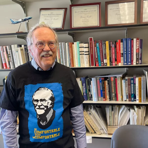 Tom Roehl smiles while wearing a t-shirt emblazoned with his smiling face and the words 'be comfortable being uncomfortable.'