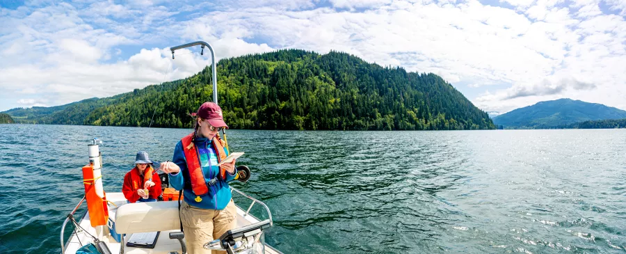 a student on a boat in the middle of Lake Whatcom consults their notes while conducting water quality testing. 