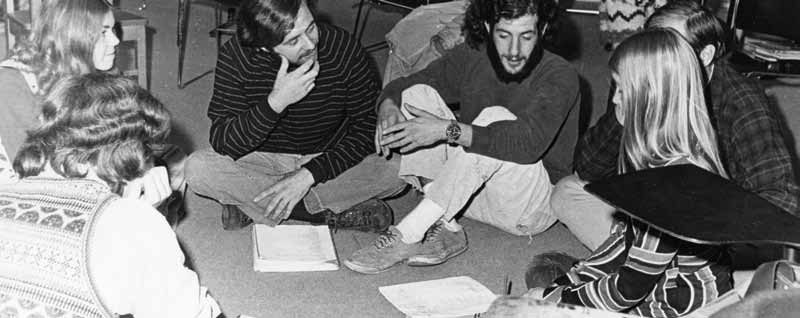 A 1970 photo of six students sitting on the floor, cross-legged, in conversation. 