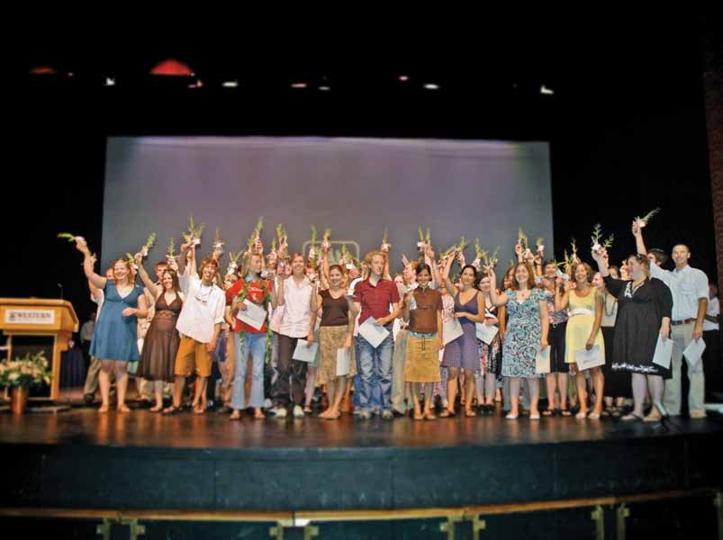 group photo of graduates standing on a stage, holding tree saplings
