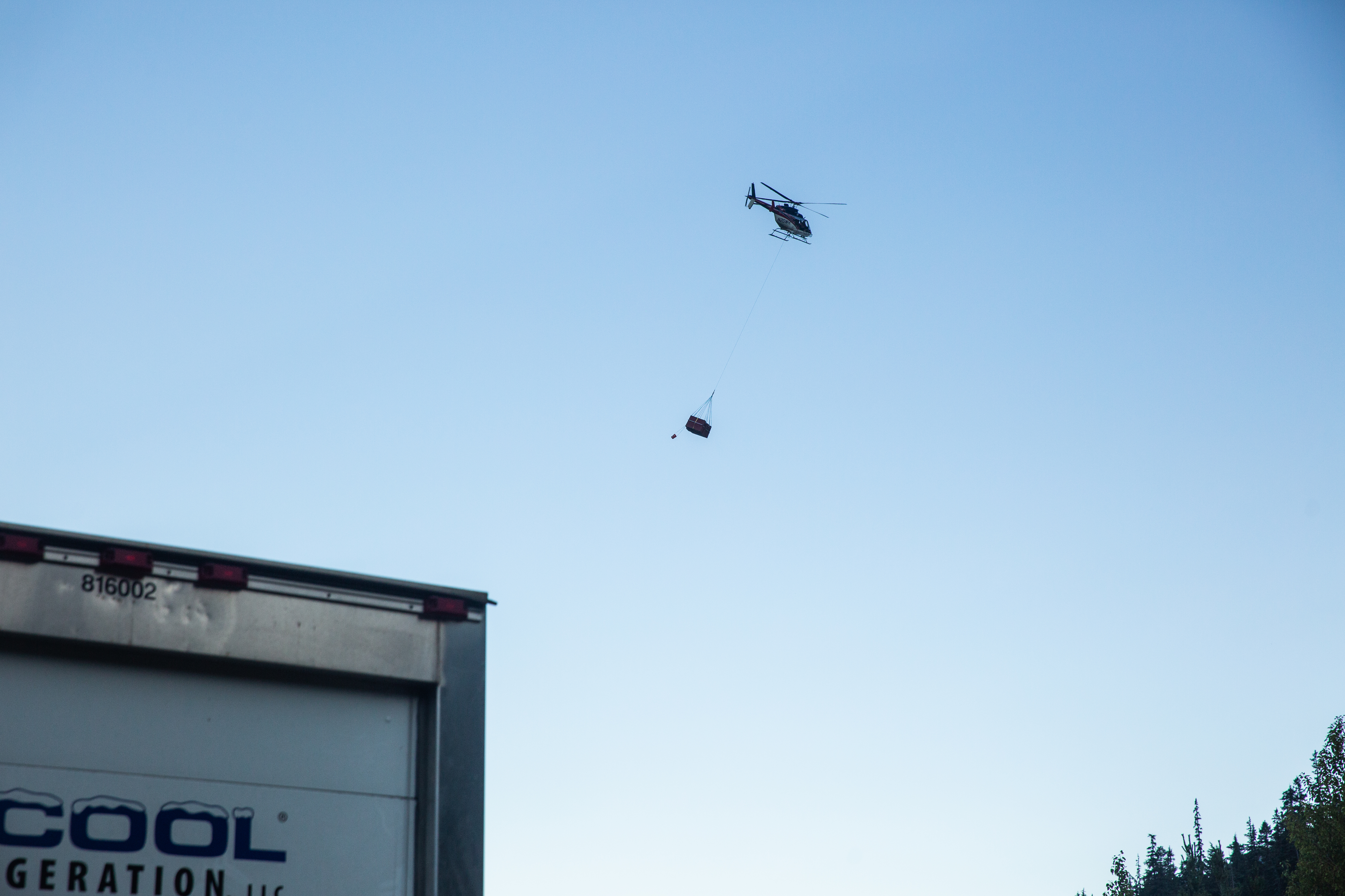 A helicopter flies away carrying three boxes with goats inside. 