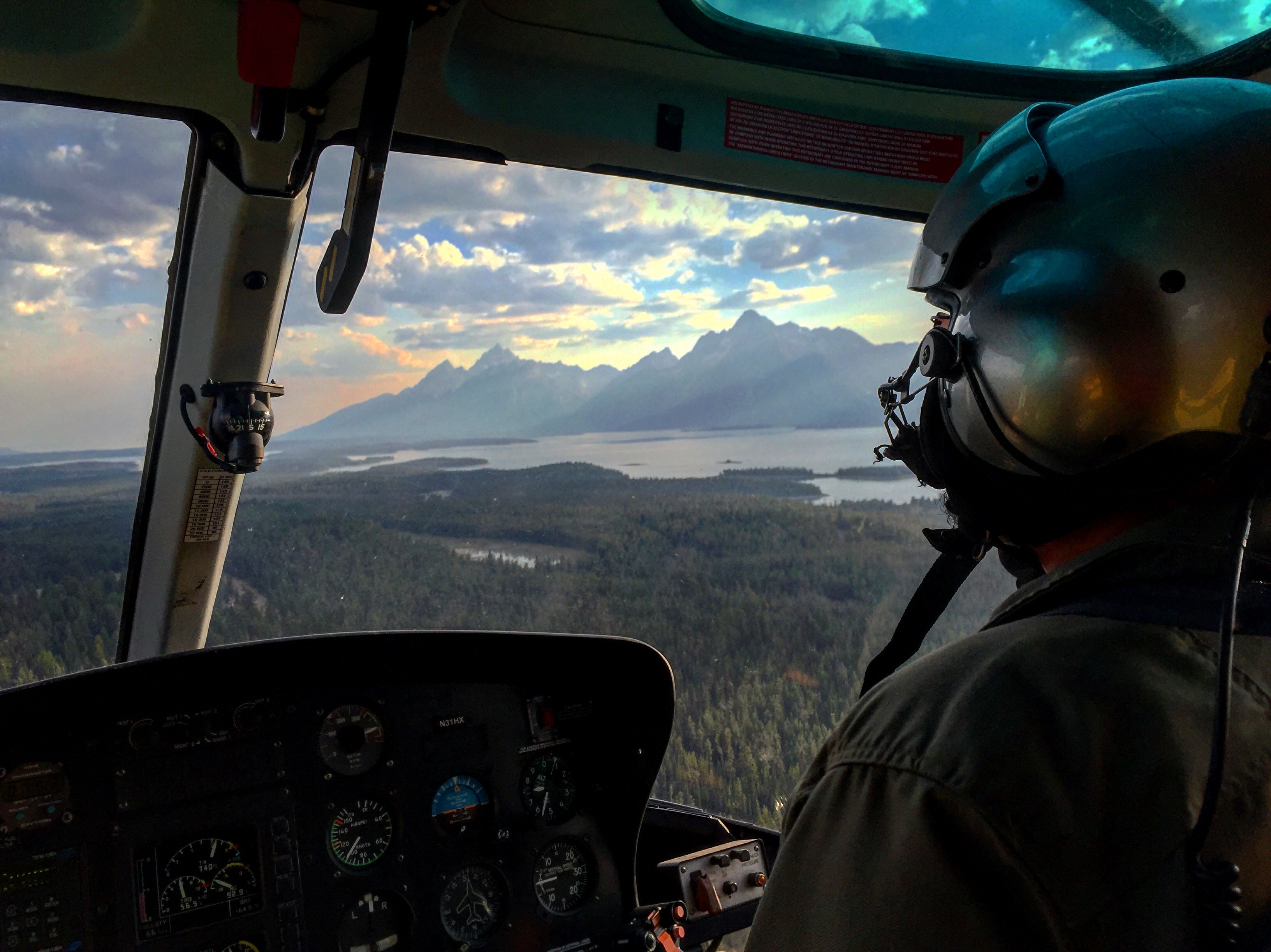 A view out the windshield of a helicopter of the Tetons, with a smoky haze in the distance. 