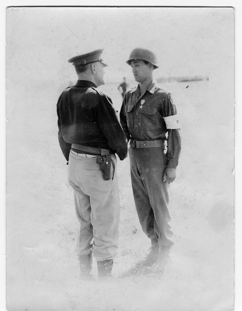 A black and white photo of a 1940s photo of a general shaking the hand of a medic wearing a silver star medal
