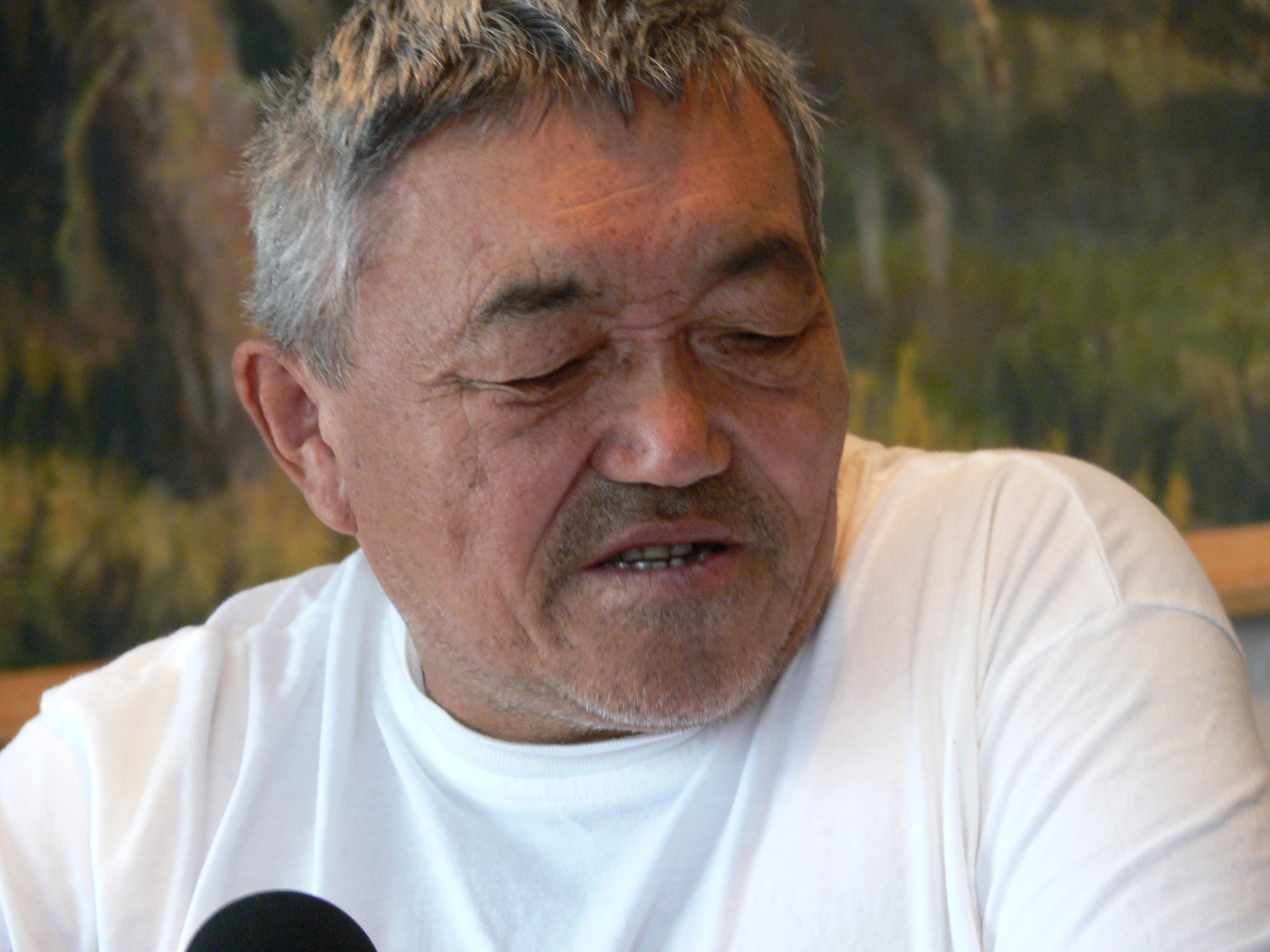 Close up of a man wearing a white t-shirt speaking into a microphone.