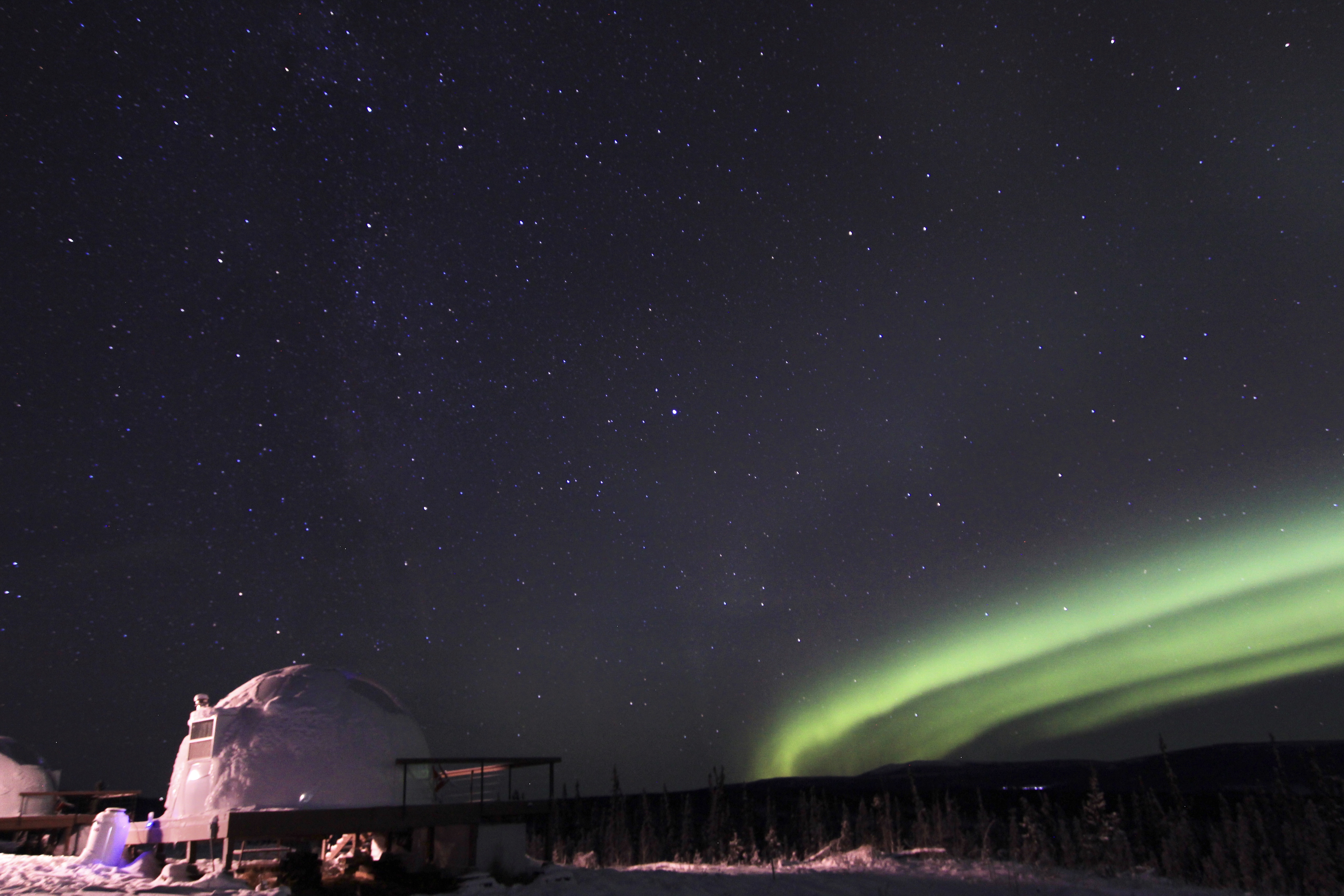 streaks of auroral light appear in a dark sky, with a dome in the foreground