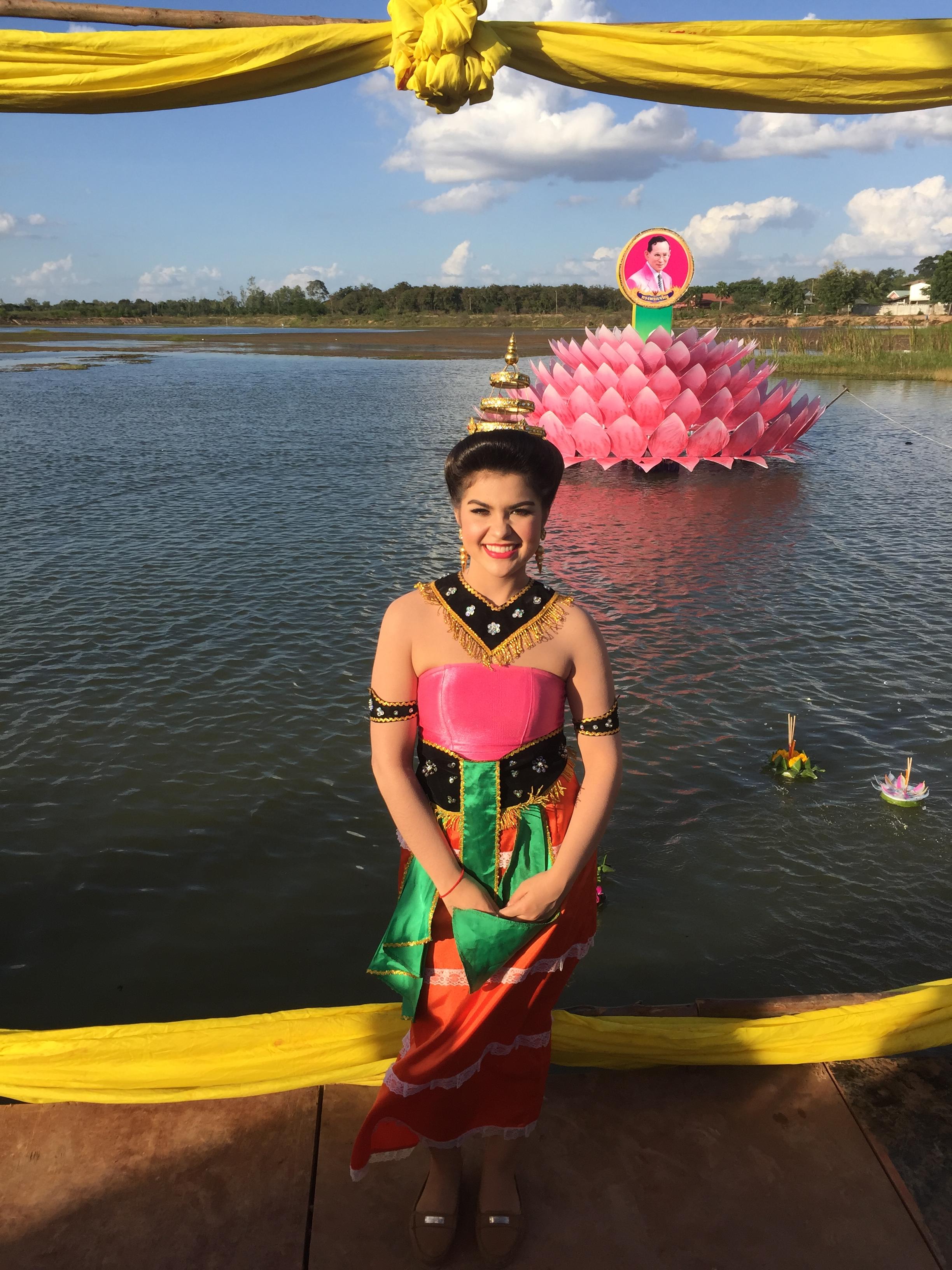 A woman in traditional Thai dress poses in front of a float on a lake.