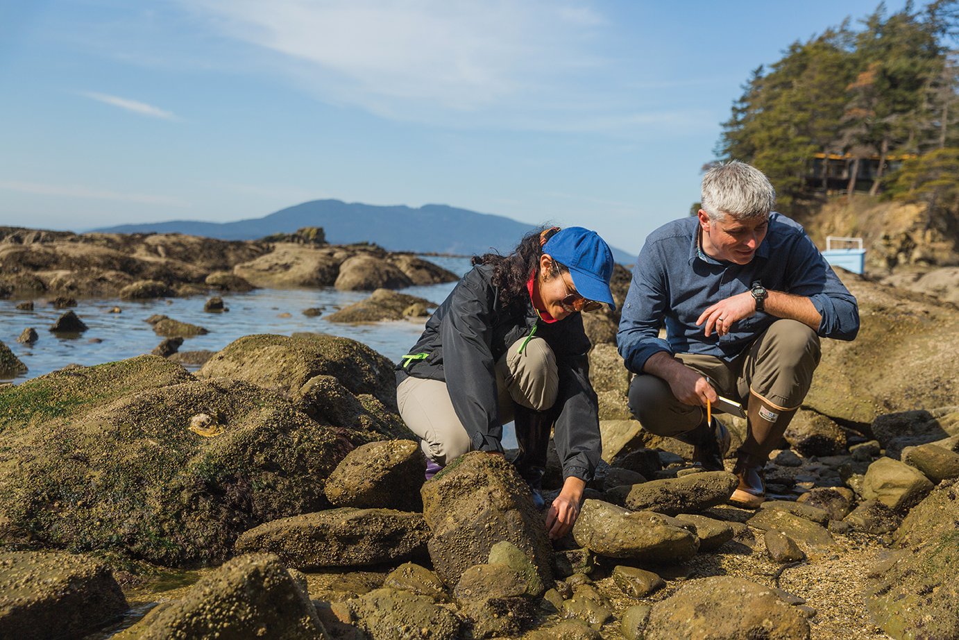 A student and professor crouch on the rocky tidelands at Larrabee State Park, collecting items for field research