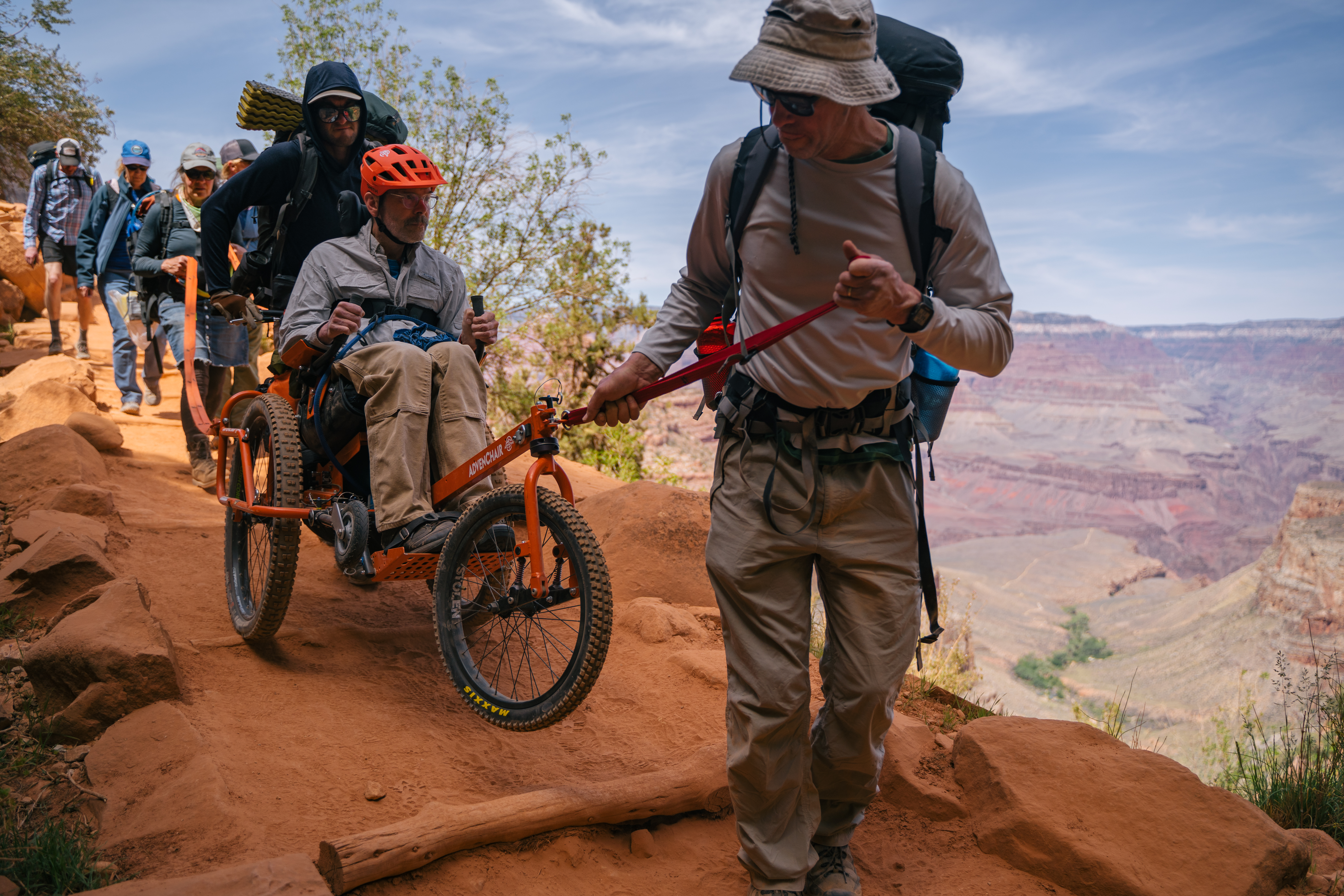 A person pulls Geoff Babb in a rugged three-legged wheelchair along a trail in the Grand Canyon