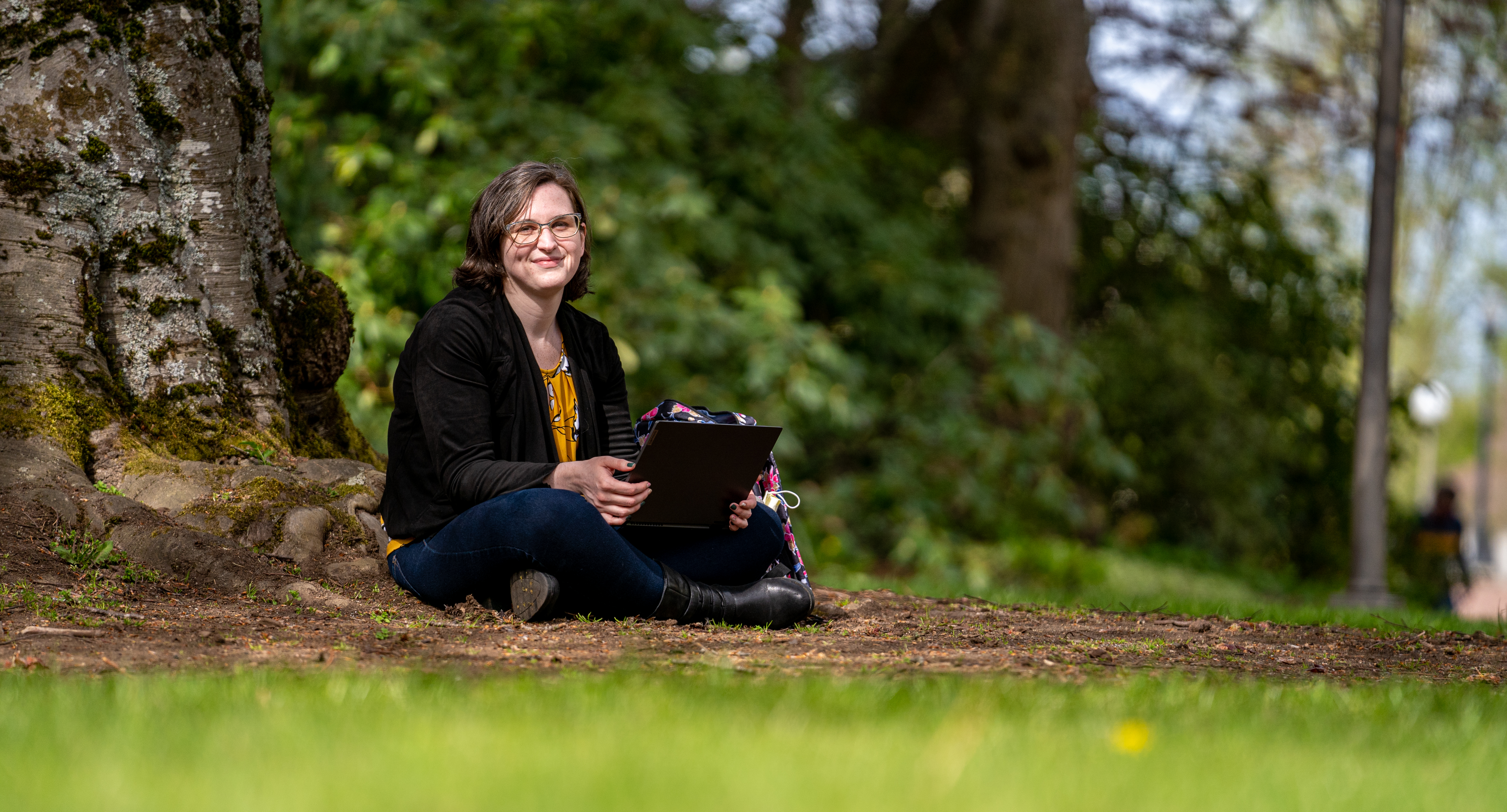 Caitlin Bannister sits beneath a tree on campus, a laptop computer in her lap