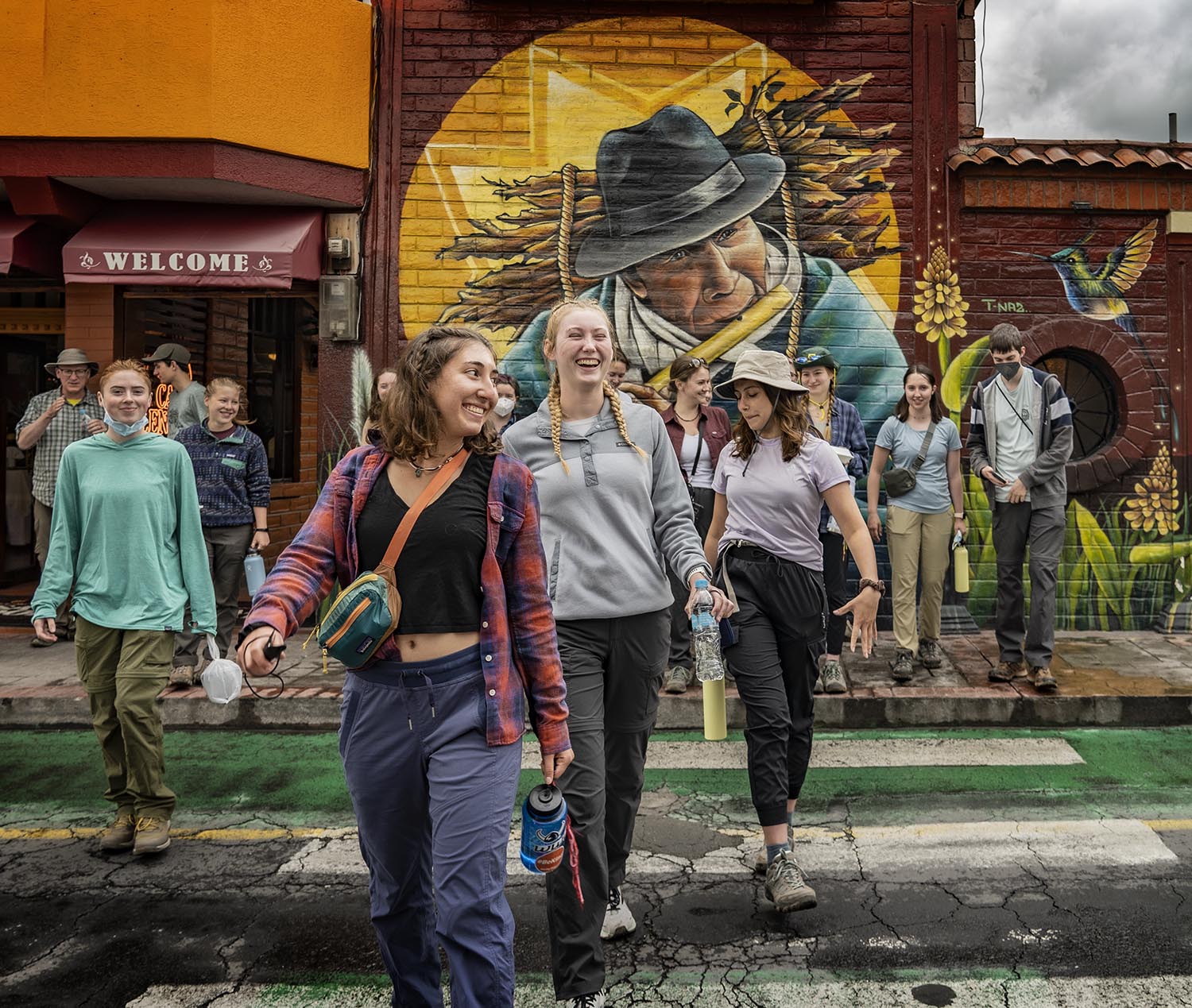 A group of Western students crossing the road, with a colorful mural of a flute player behind them
