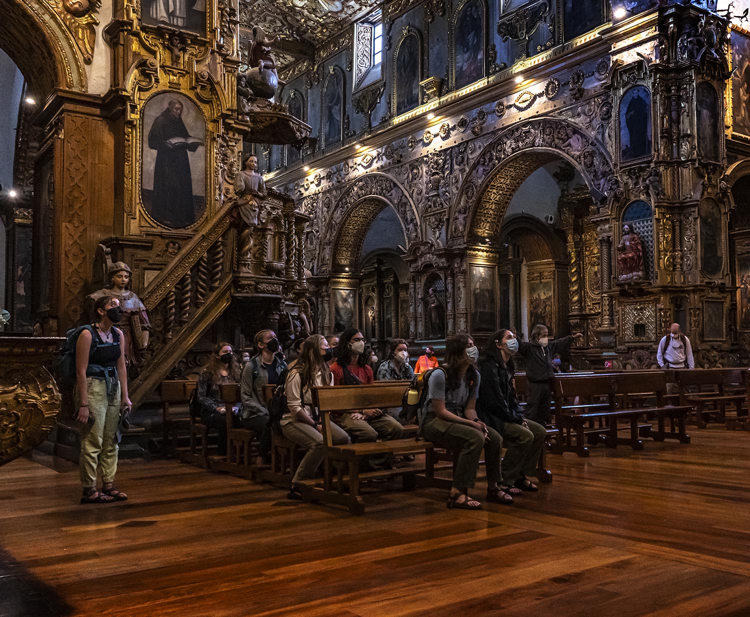 Students seated in pews, looking up at the ornate decorations inside of a church