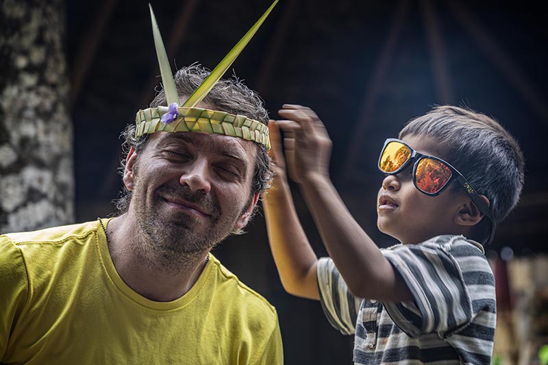 Story photographer Sean Patrick being adorned in a woven headband by a little boy wearing sunglasses, which are too big for him and crooked on his face