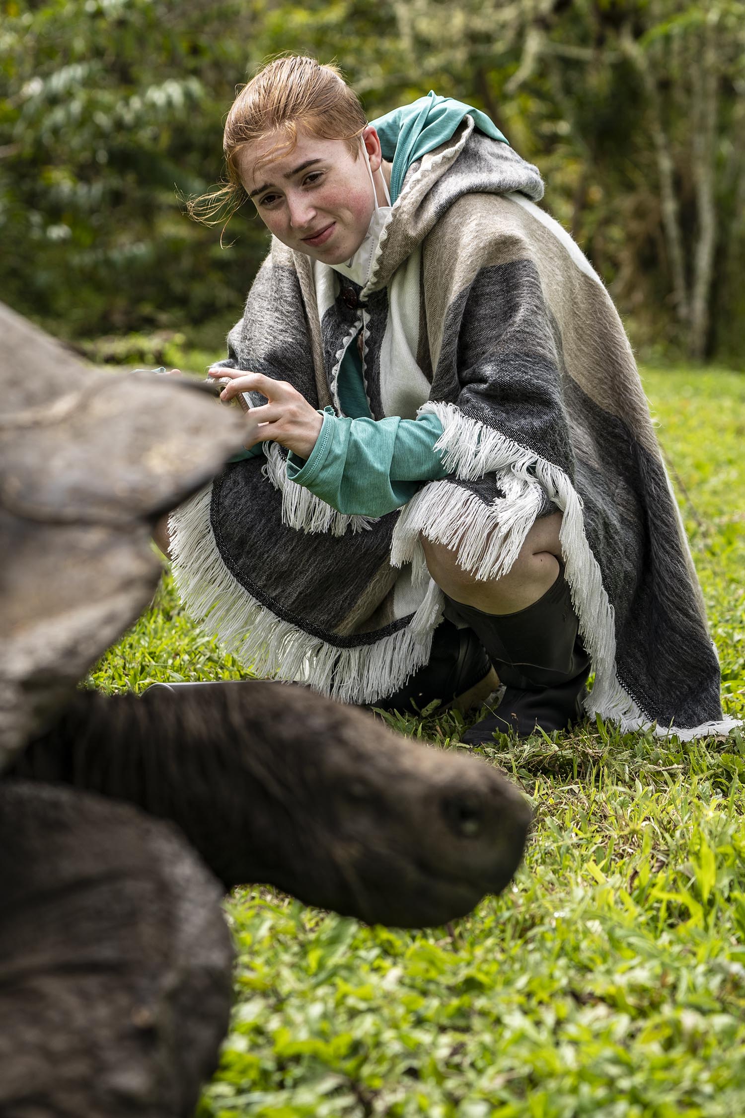 A student wearing a hooded cape crouches down to observe a tortoise