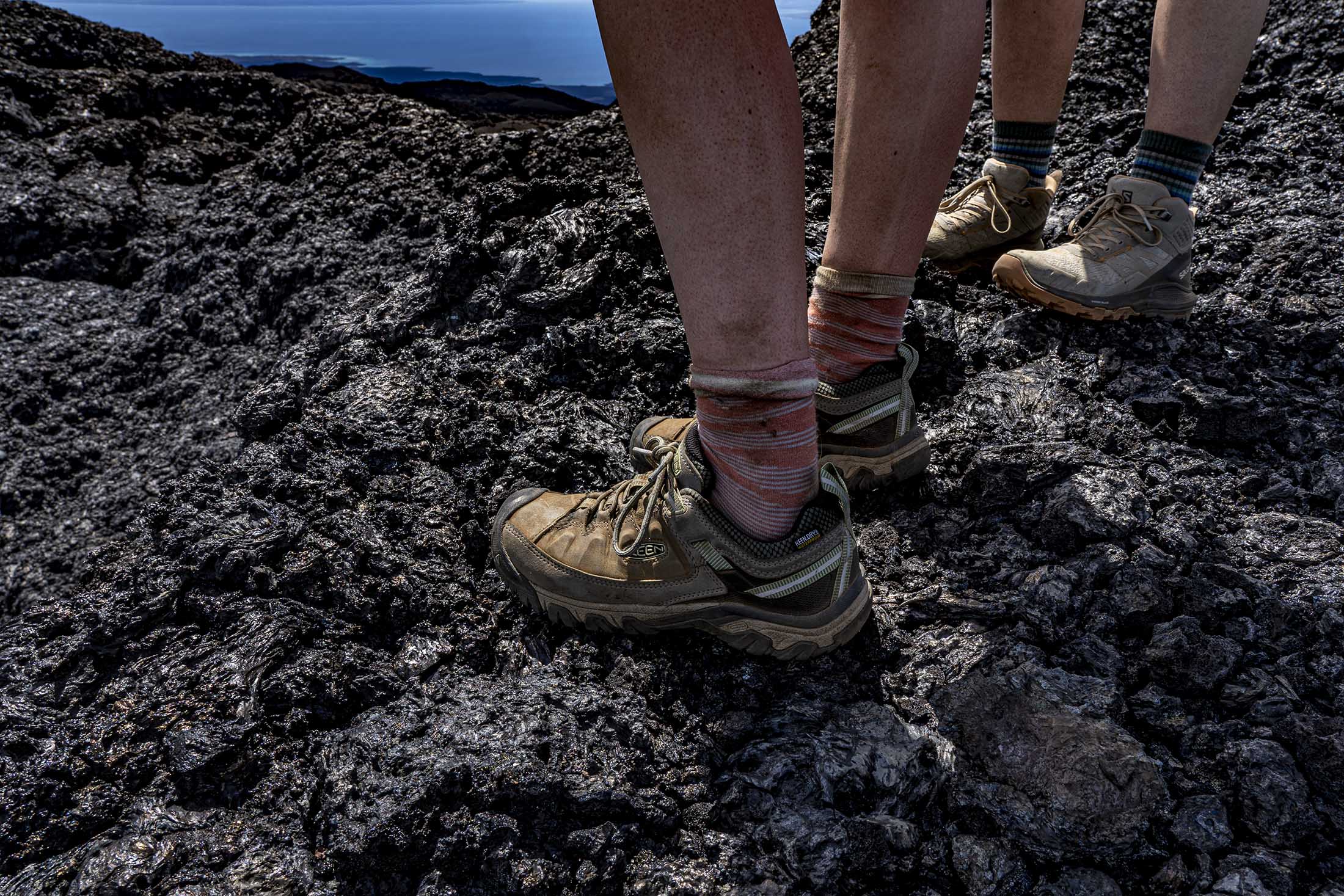 Close up of two people's lower legs standing on craggy rocks. Both are wearing hiking shoes and short striped socks, and have smudges of dirt on their calves as though they've been hiking.