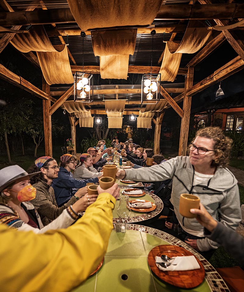 Students cheersing at a long table, outside at night under a wooden structure with warm lighting