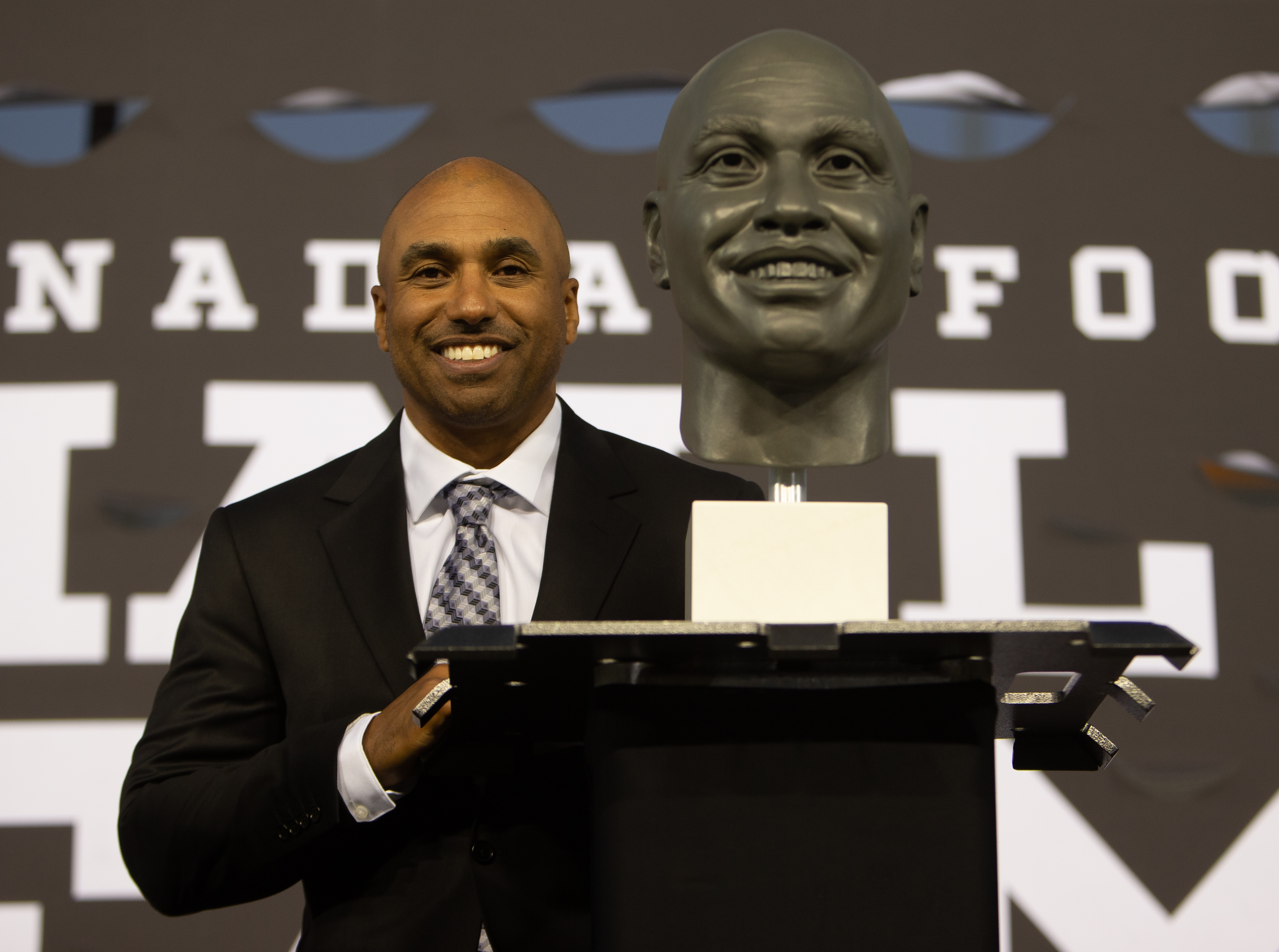 Orlondo Steinauer stands at a podium, smiling, next to a bust of himself