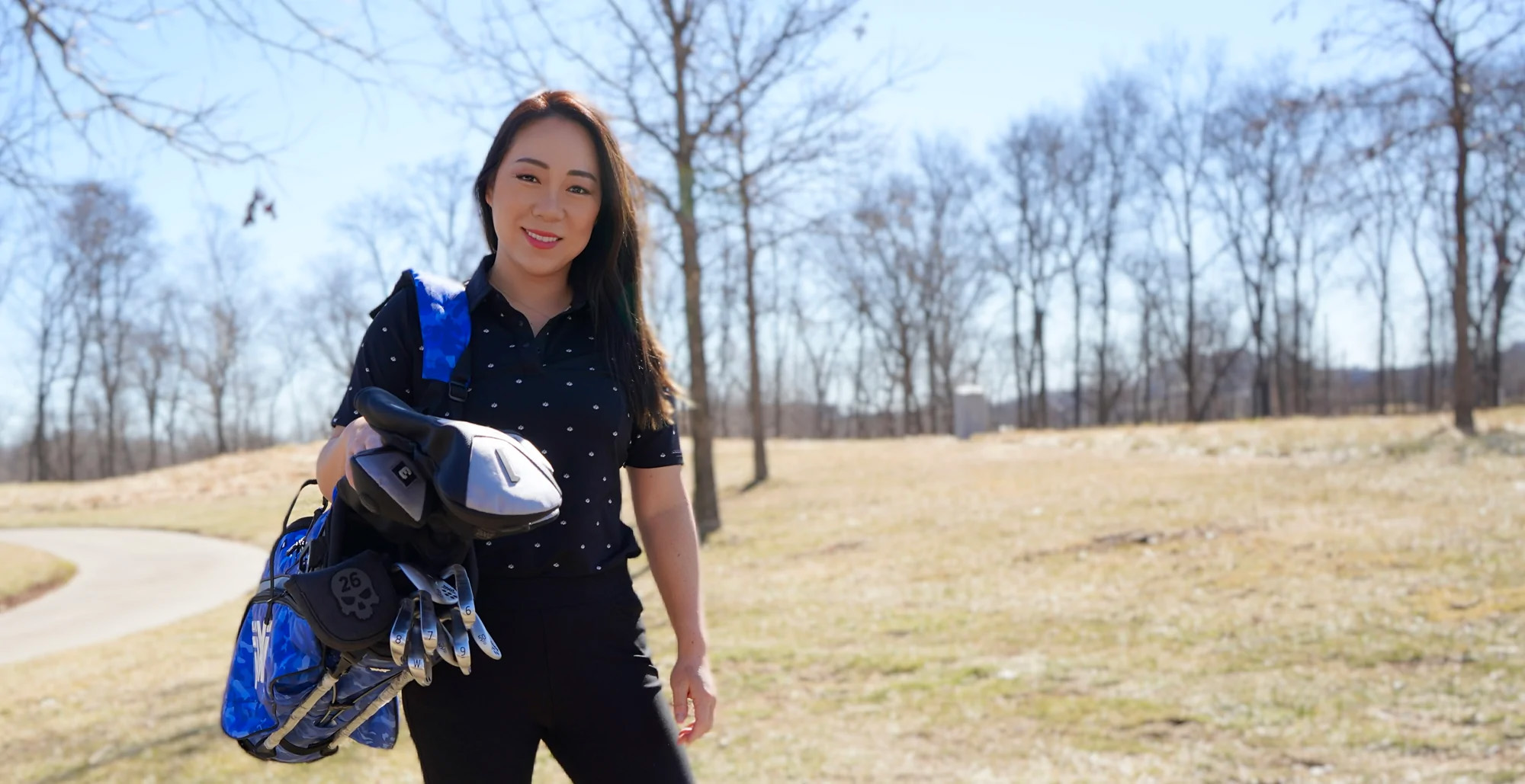 Cathy Kim stands on a golf course, a golf bag and clubs over her shoulder