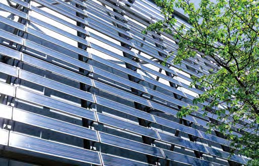 rows of solar panels line the outside of a building, next to a leafy green tree