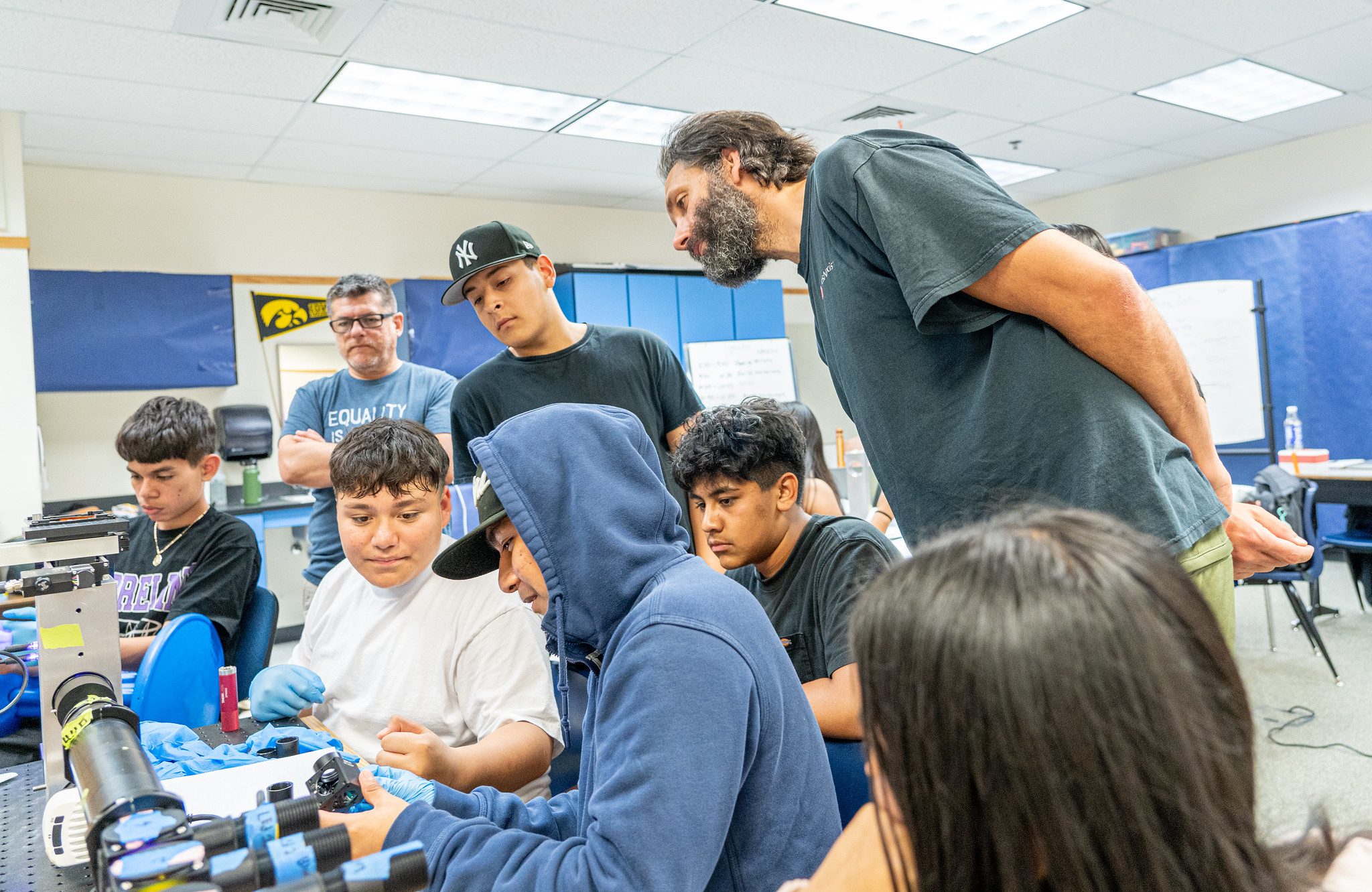 A teacher leans over the shoulders of a group of students working at a lab bench