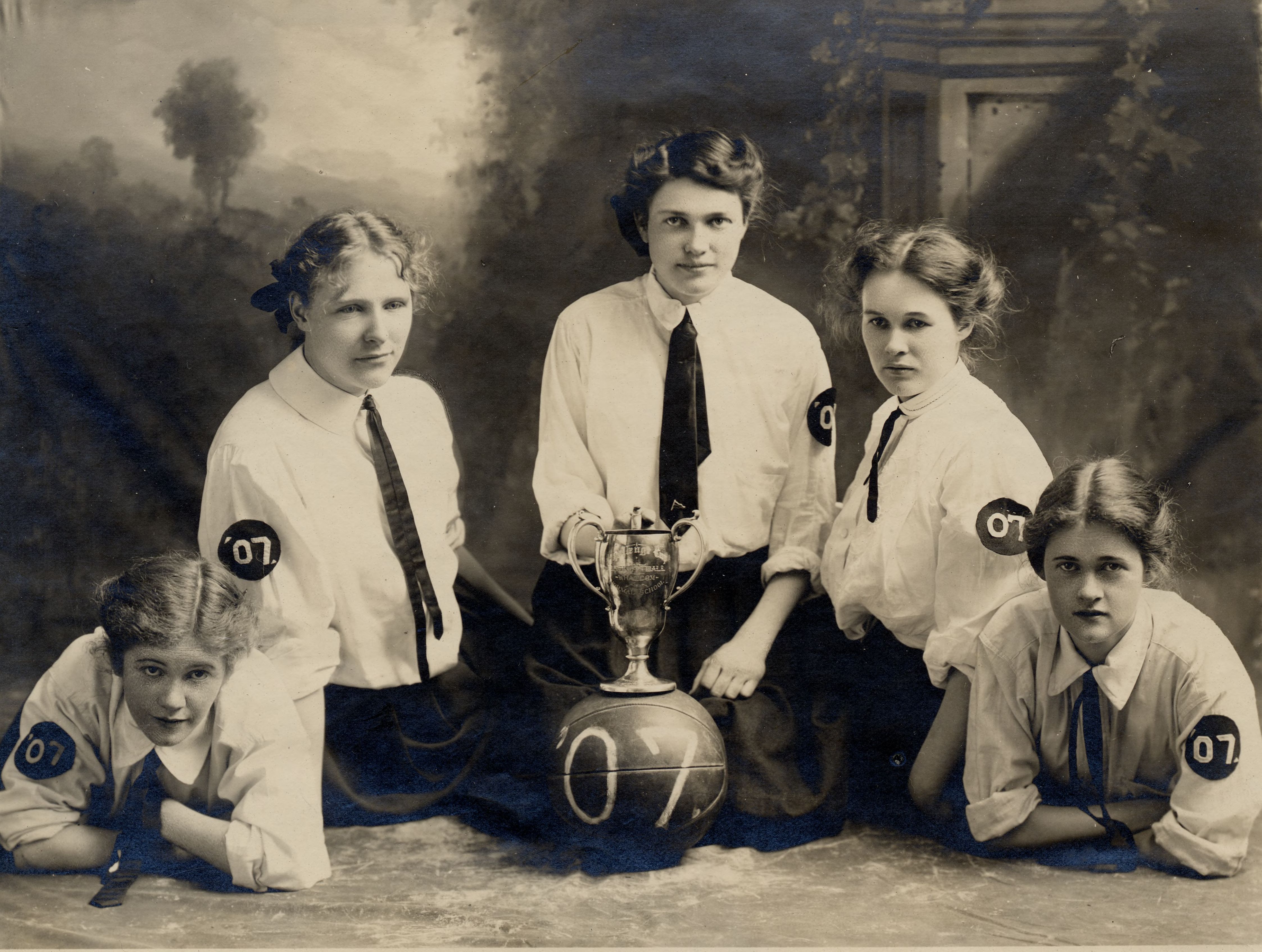 1906 women's basketball team portrait, displaying a gold trophy cup
