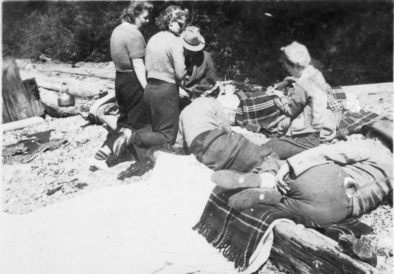 several women recline in the sun on a rocky beach in 1940