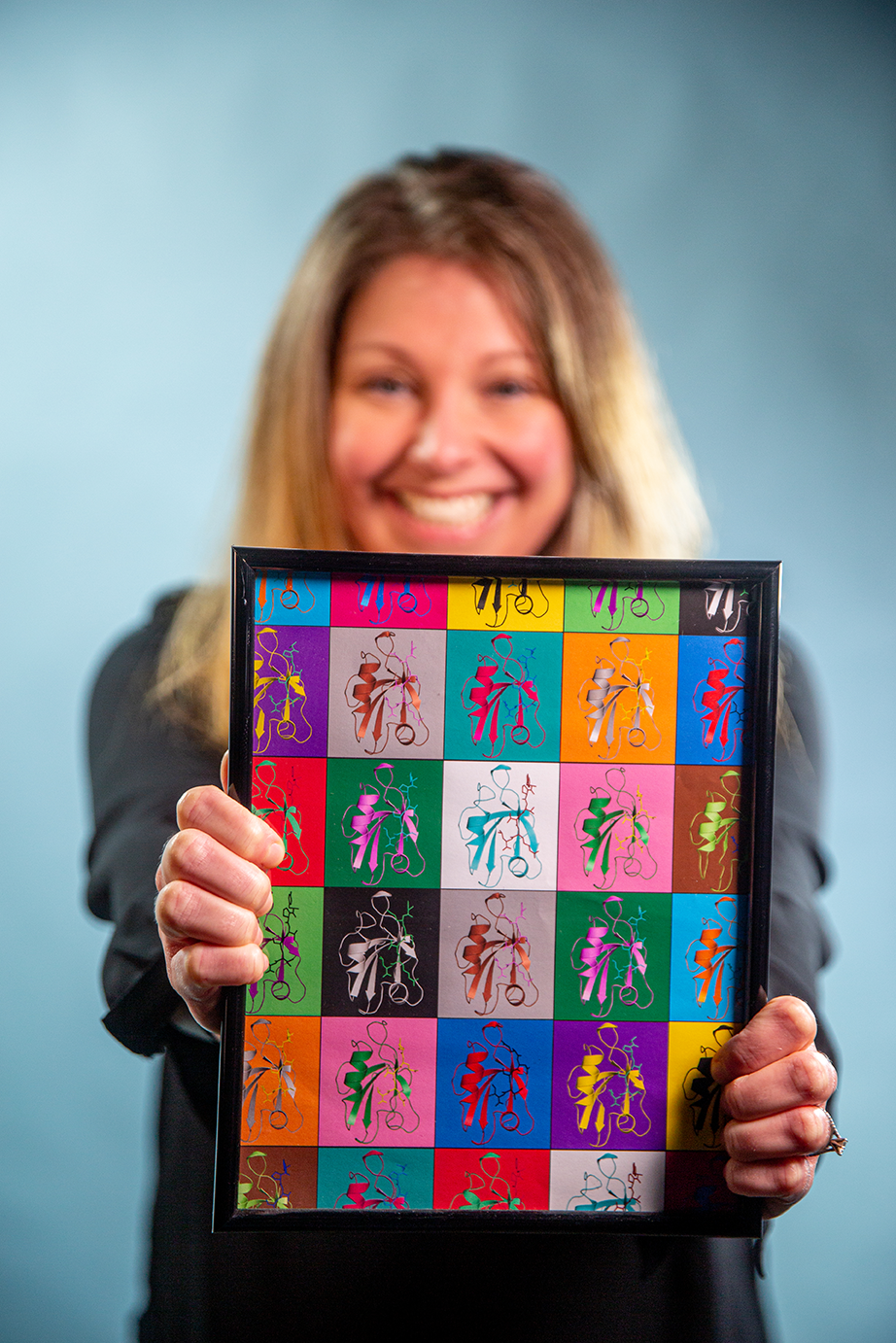 Jeanine Amacher holds an image with a grid of colorful depictions of proteins