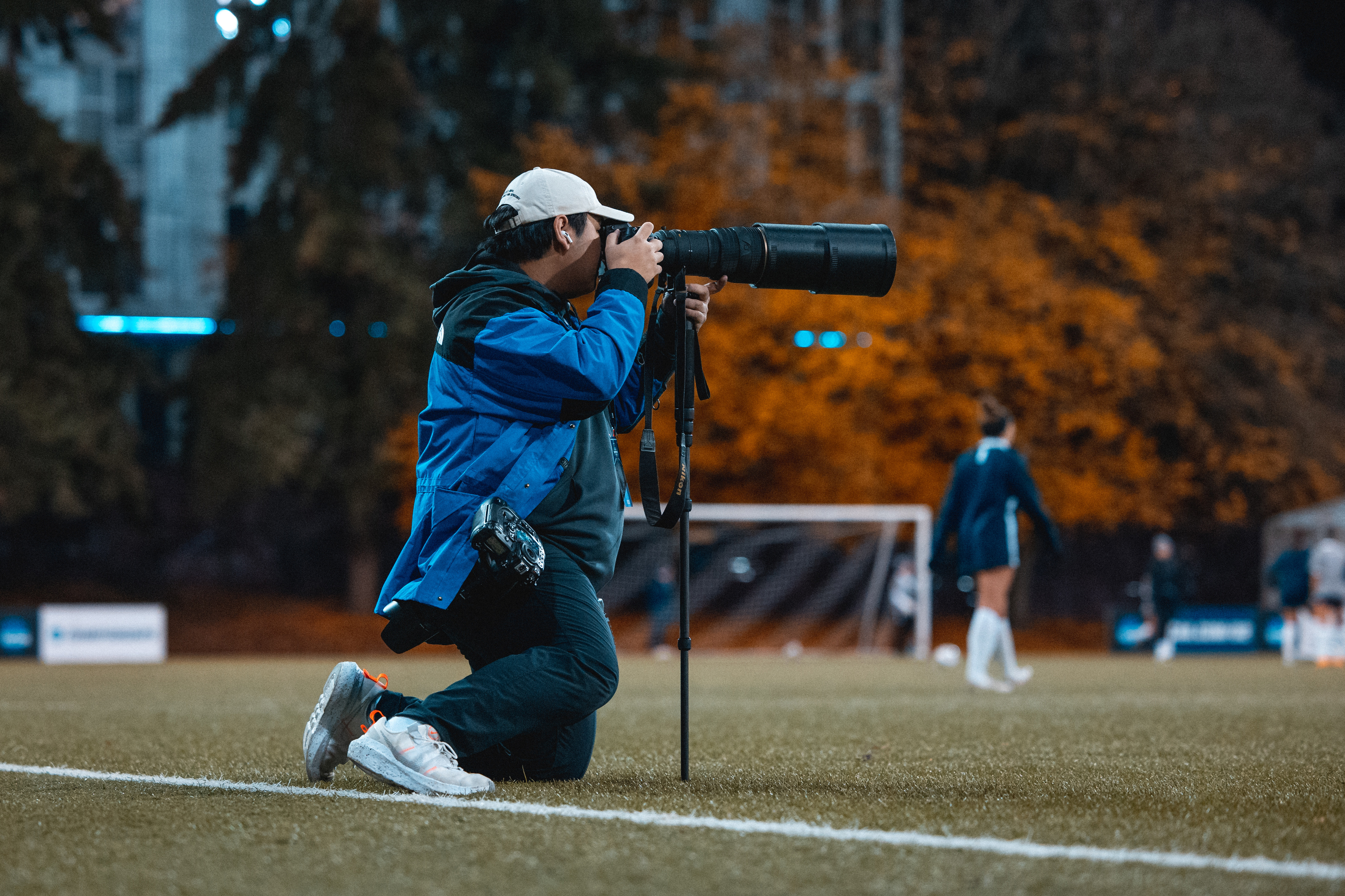 Eric Becker kneels on the sidelines as he photographs the action with a long lens.