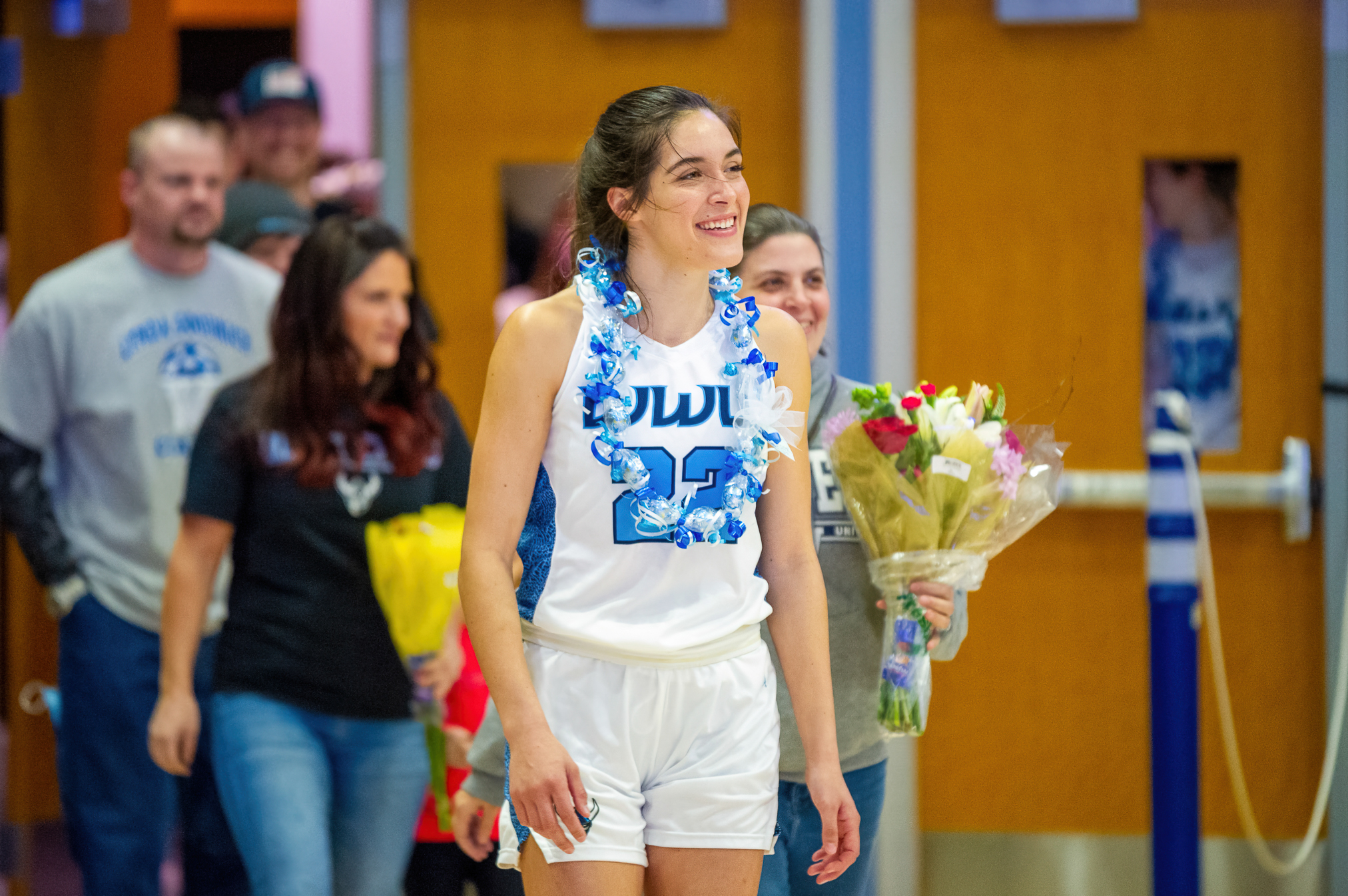 Gracie wears a lei and smiles as she walks onto the court before a game. 
