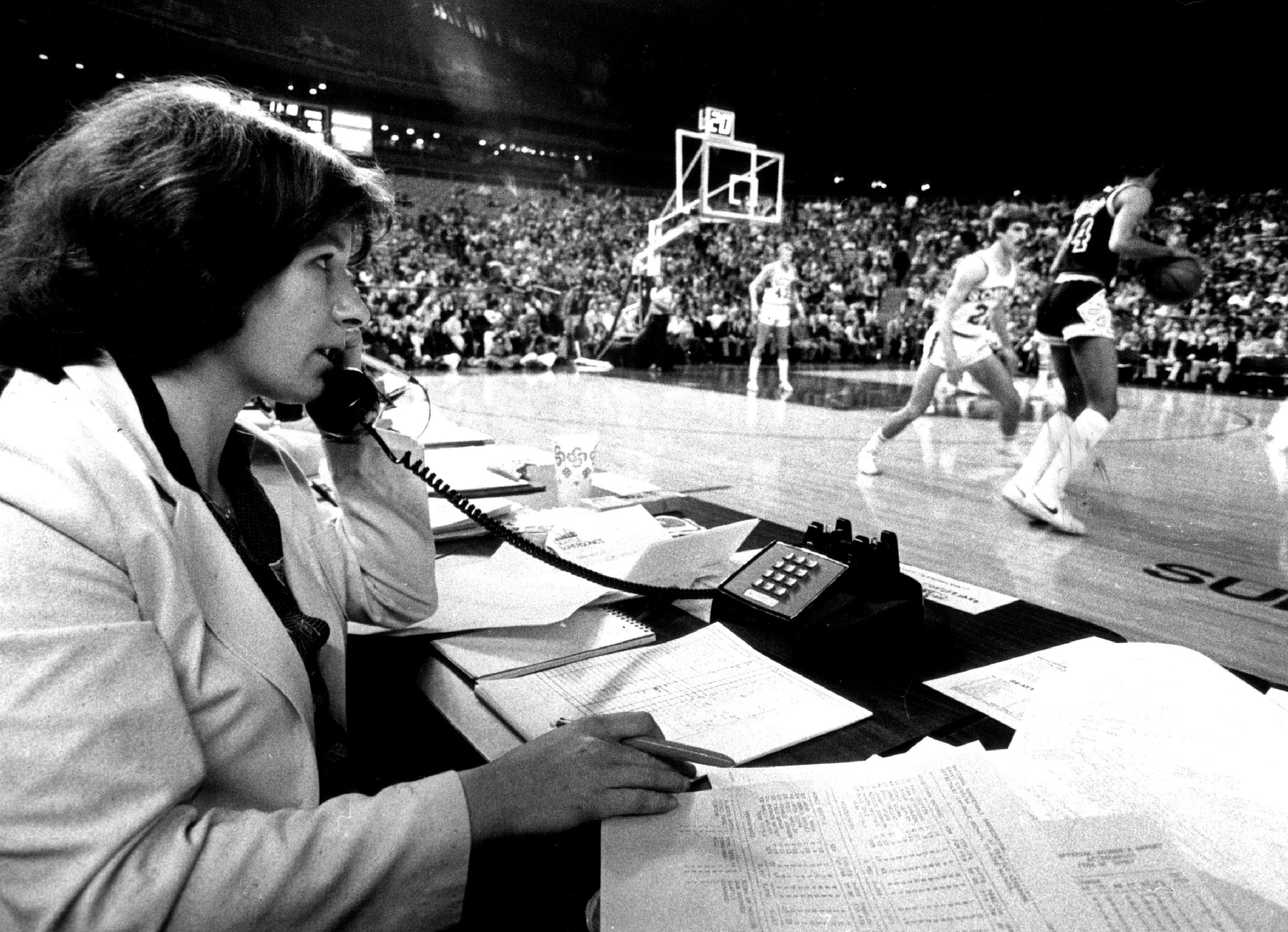 A woman sits at a table and talks on a corded telephone while at courtside during a professional basketball game