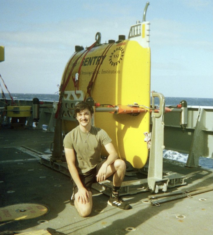 Dexter Davis on a research ship with a remotely piloted submarine behind him.
