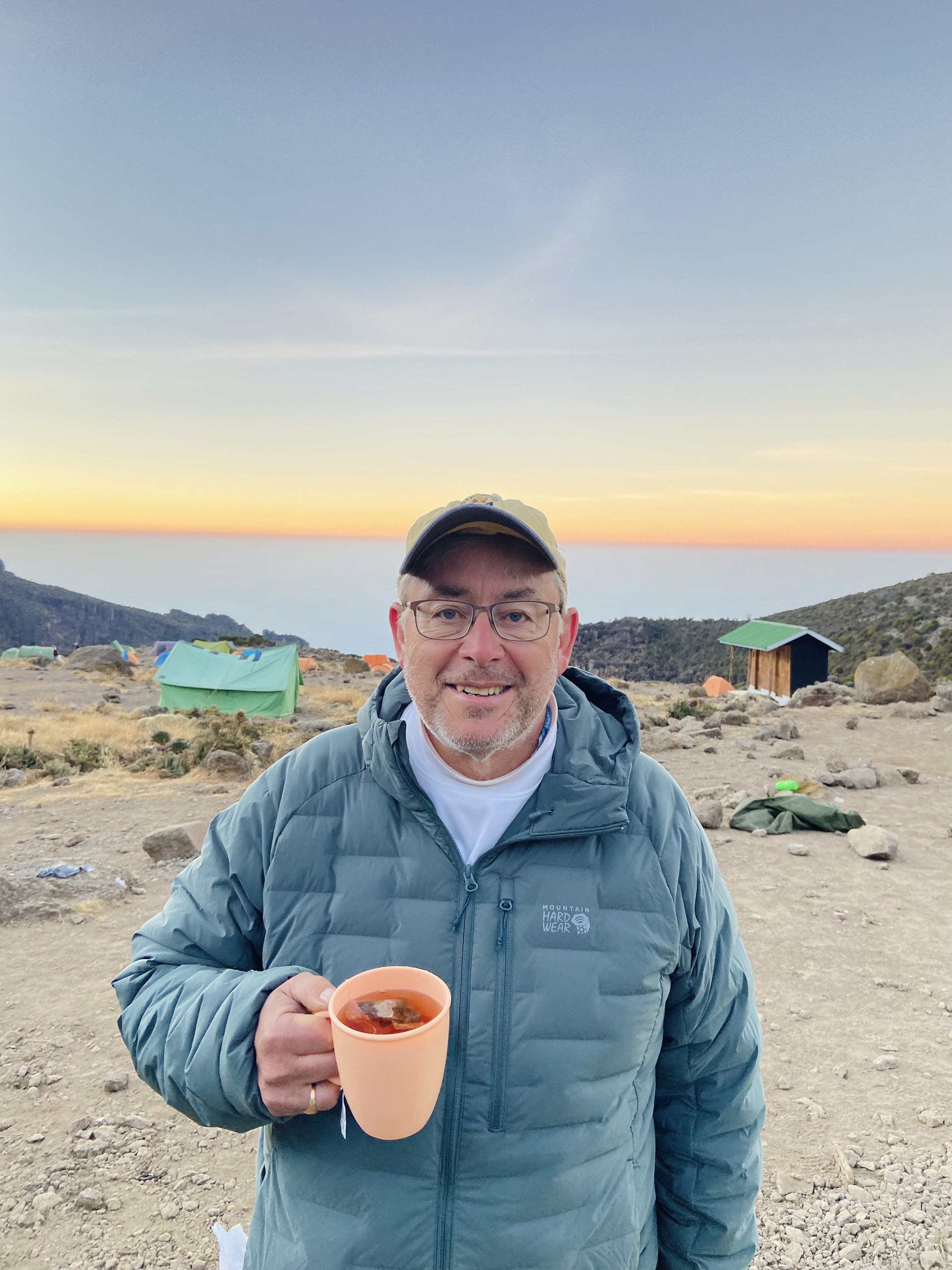 Larry Orman stands on the top of a mountain at sunrise, holding a cup of tea