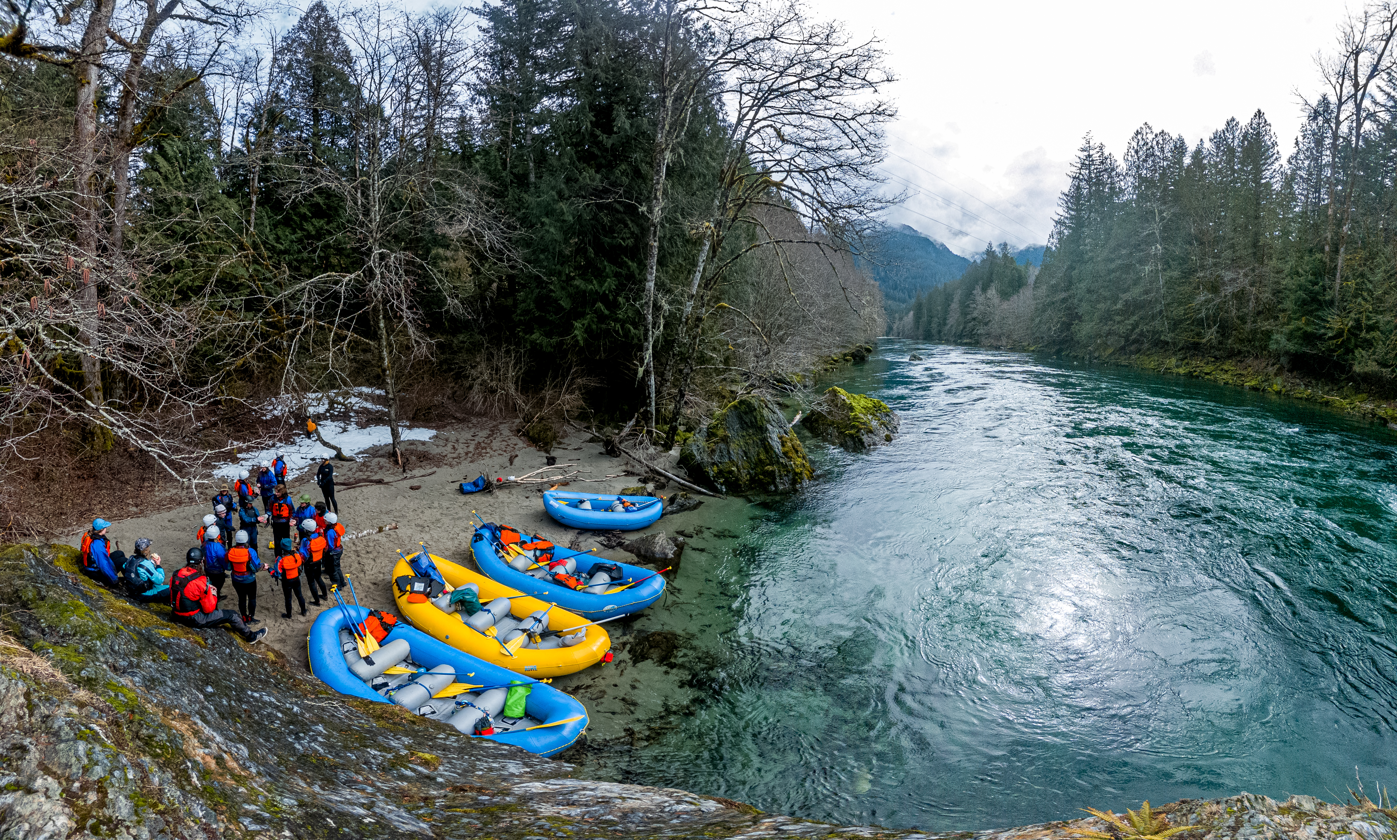 Colorful rafts on the riverbank contrast with the blue-green glacier-melt water while the group gathers before heading out. 