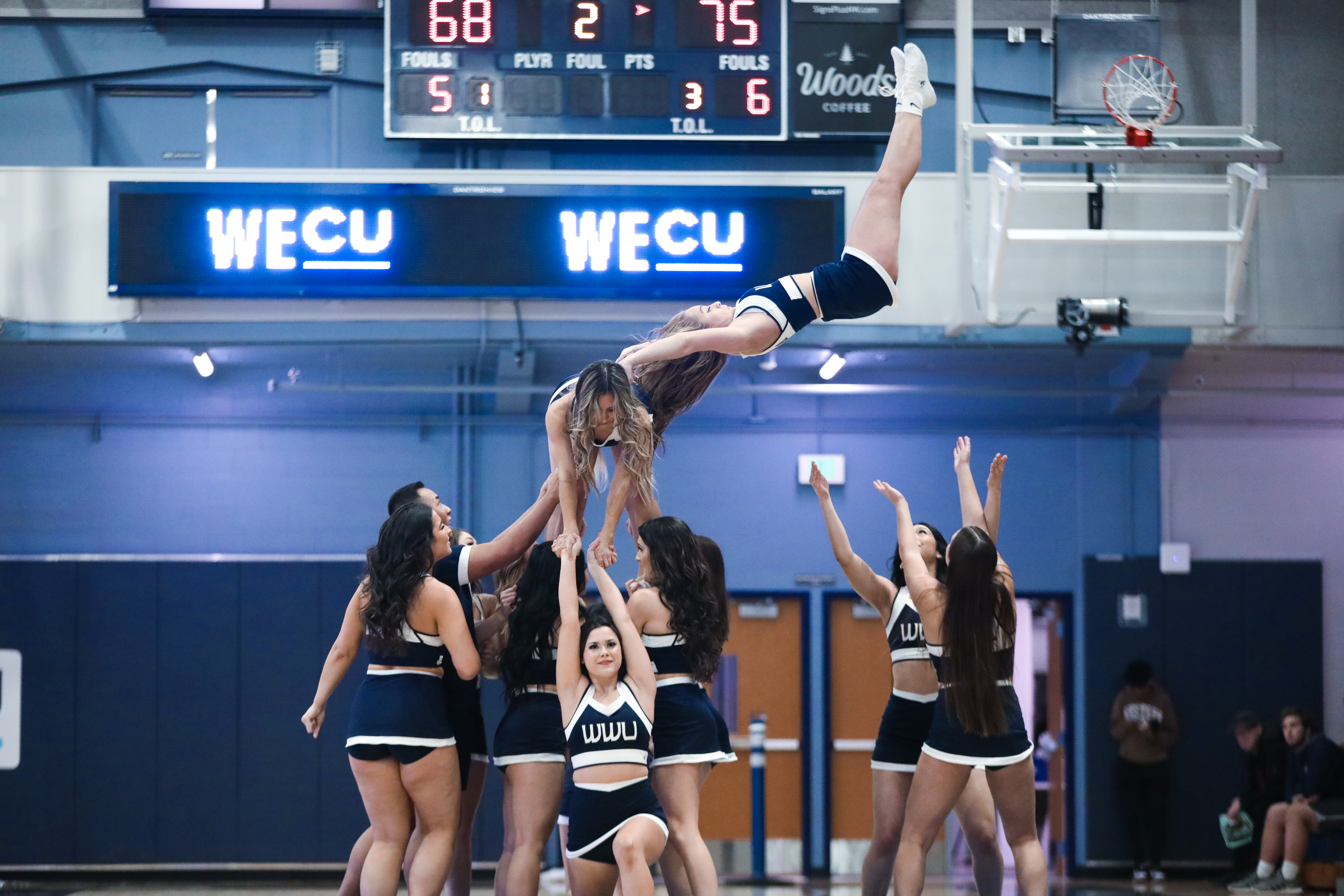 Cheerleaders perform a group tumbling routine with one in the midst of dropping from a handstand at the top of a human pyramid into the arms of teammates. 