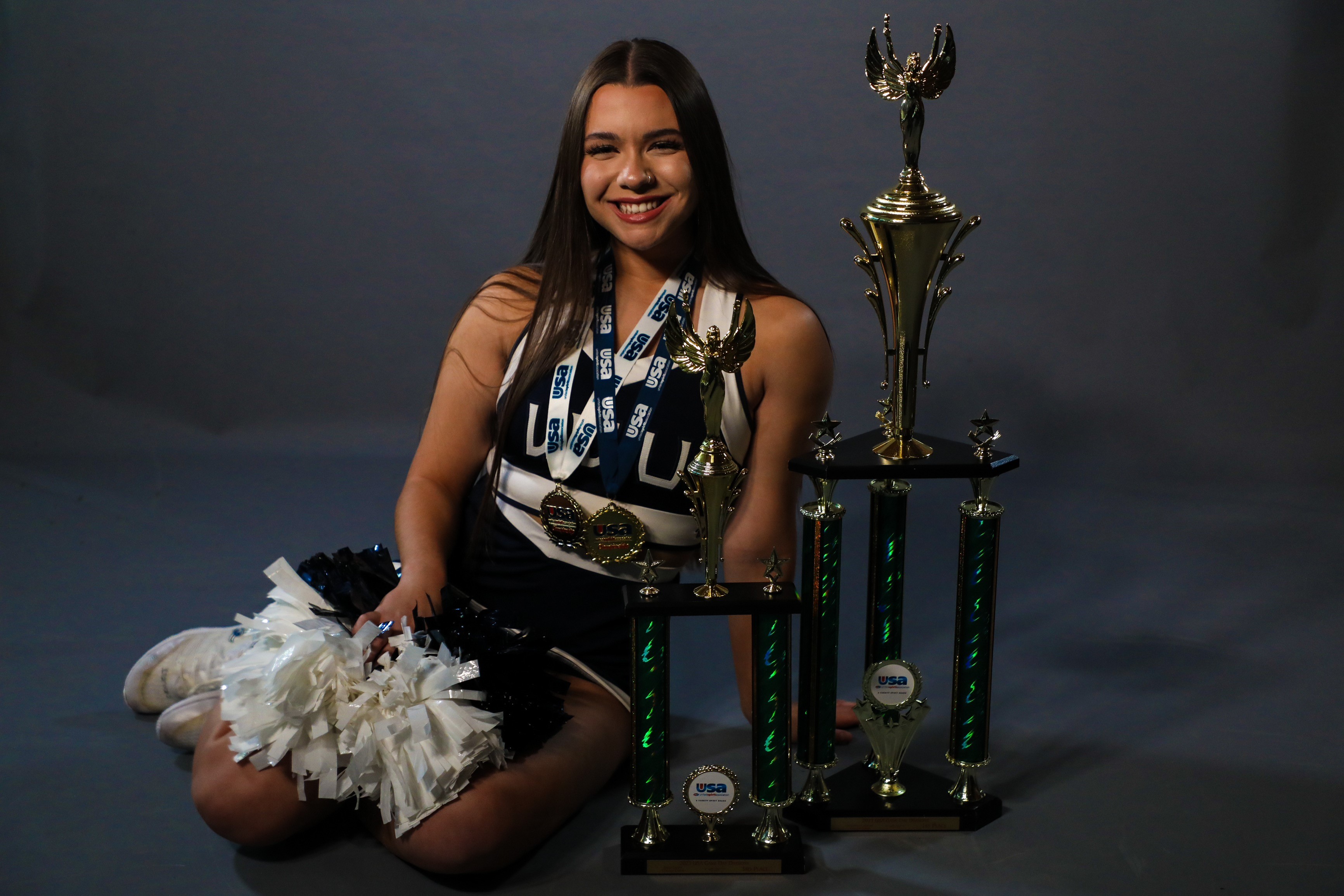Amirah Casey, in her cheer uniform, sits next to a gigantic trophy