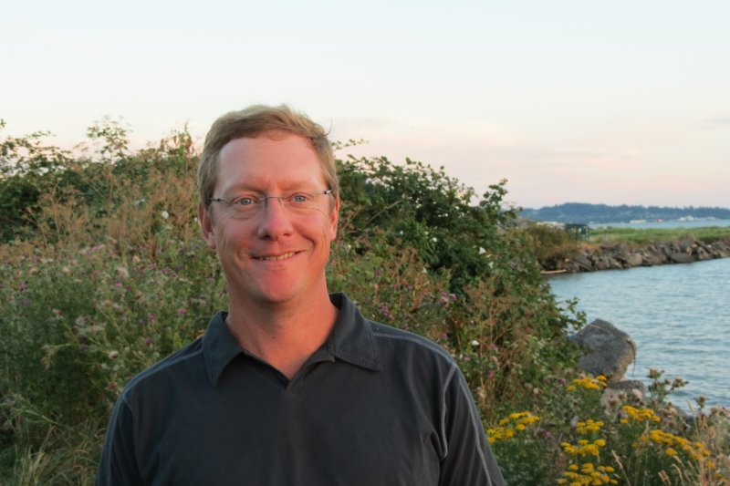 Keith Russell stands on a hillside next to the water at sunset 