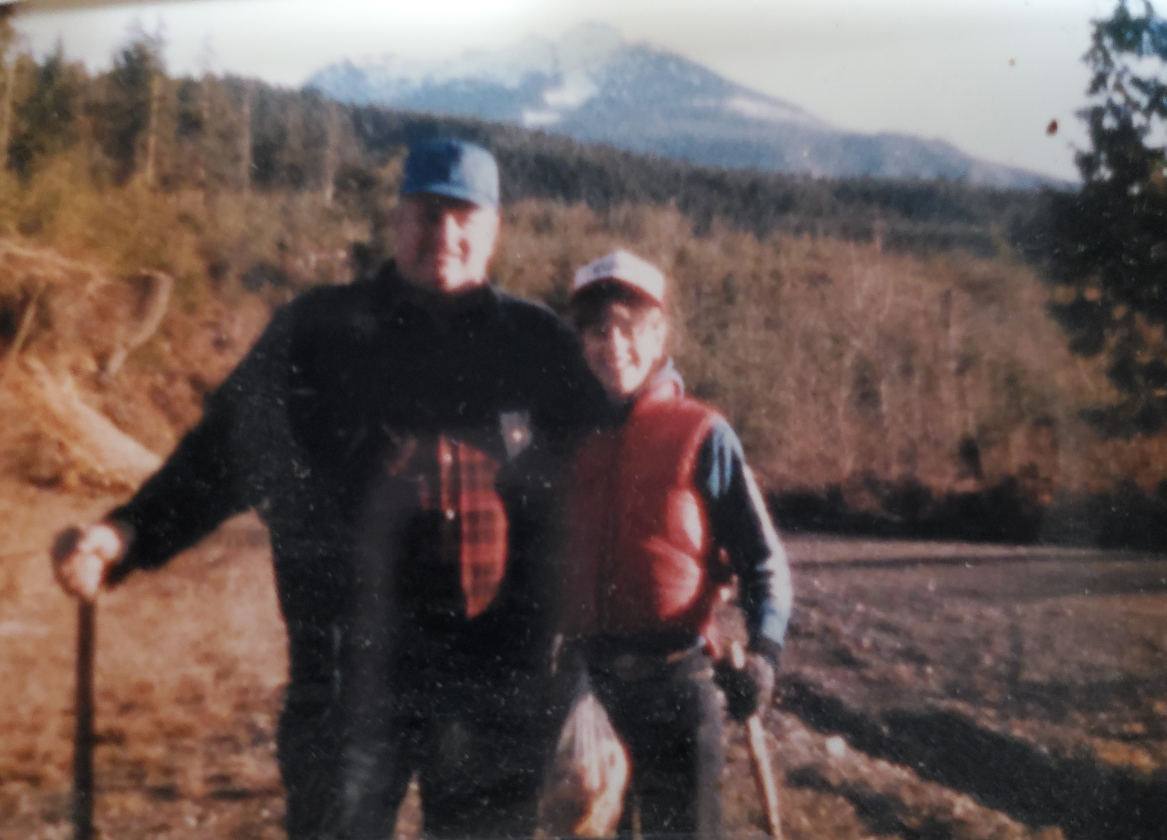 John and Julann Spromberg on a wooded riverside, holding hiking sticks and smiling