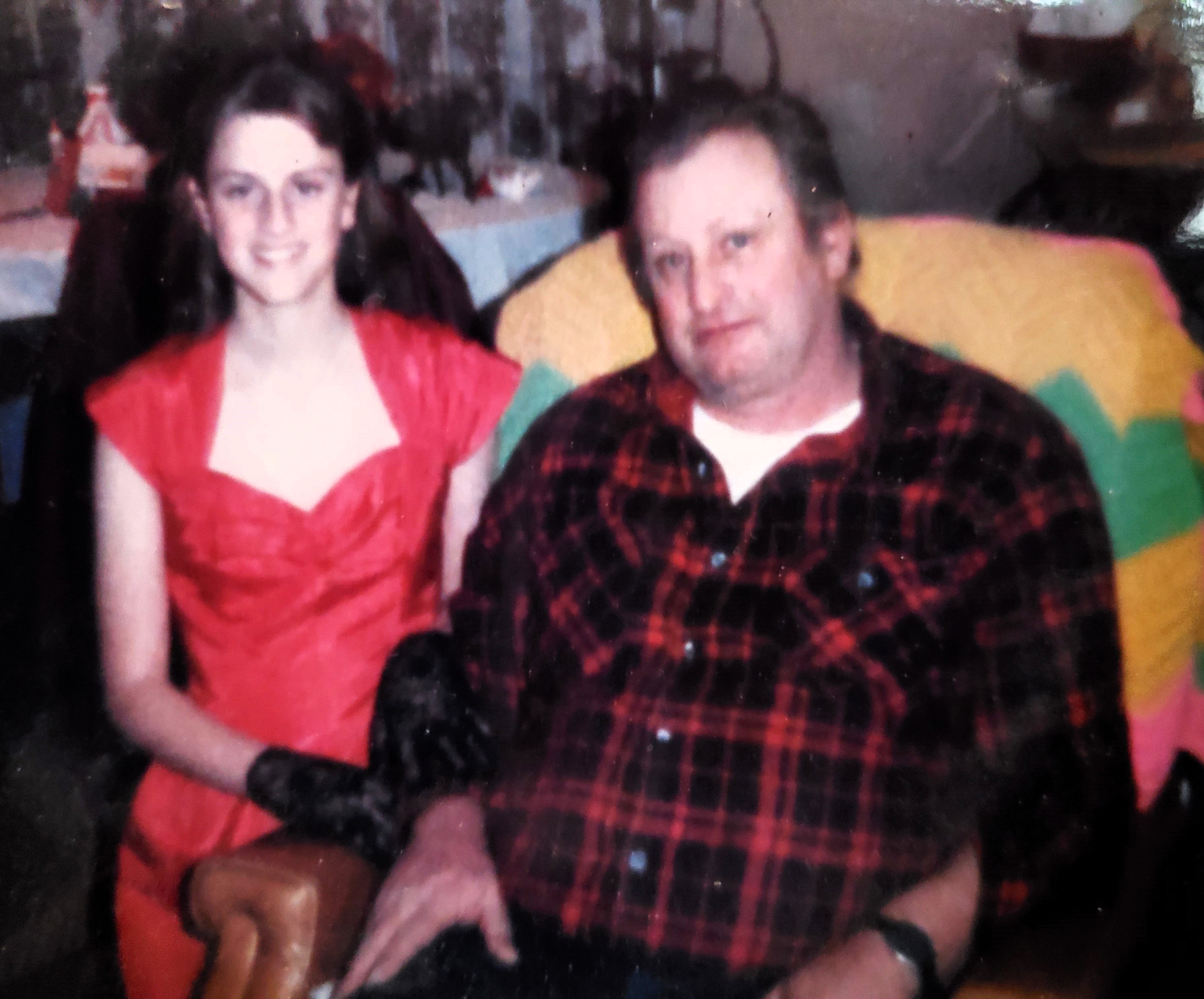 a teenager in a formal red dress and black gloves sits next to a man wearing a red and plaid flannel shirt