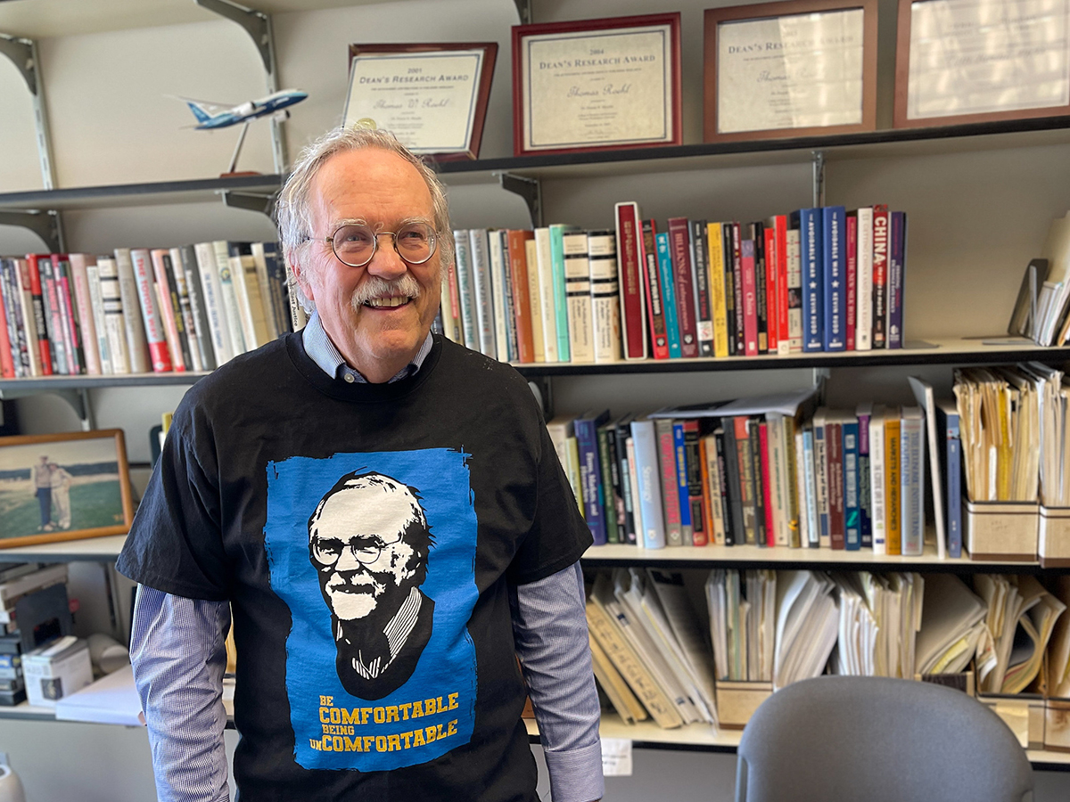 Tom Roehl smiles while wearing a t-shirt emblazoned with his smiling face and the words 'be comfortable being uncomfortable.'