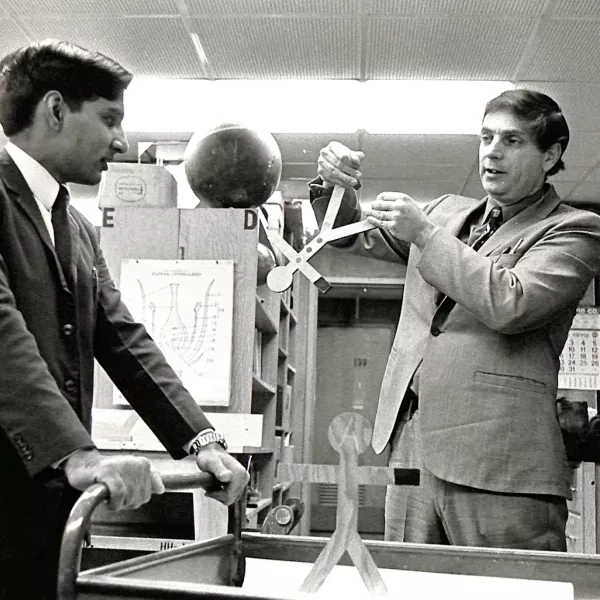 1972 photo of Piyush Swami and Irwin Slesnick chatting among shelves filled with books and teaching supplies 