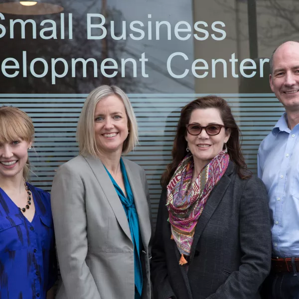 Four people standing in front of a window with lettering that says &quot;Small Business Development Center&quot;