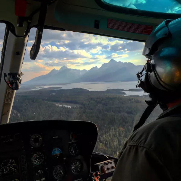A view out the windshield of a helicopter of the Tetons, with a smoky haze in the distance. 