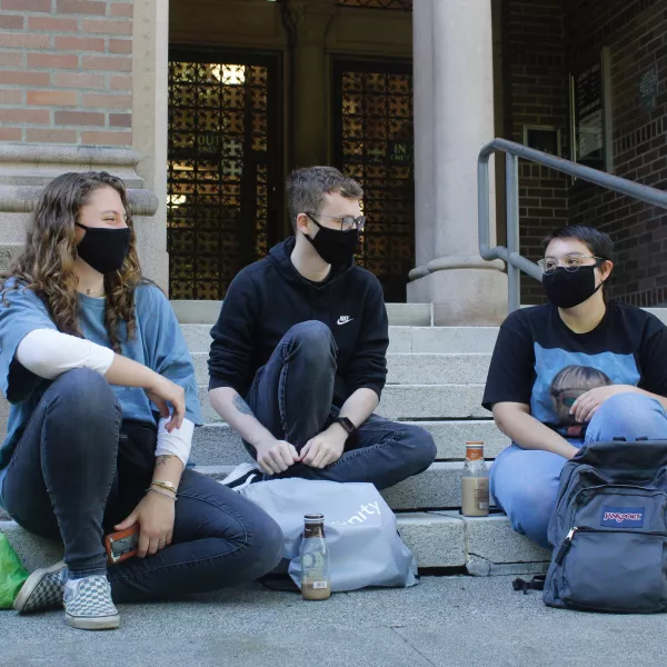 Three masked students sit on the steps of Wilson library 