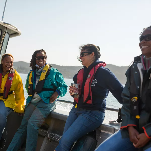 four smiling women lean against the railing of a boat on the bay