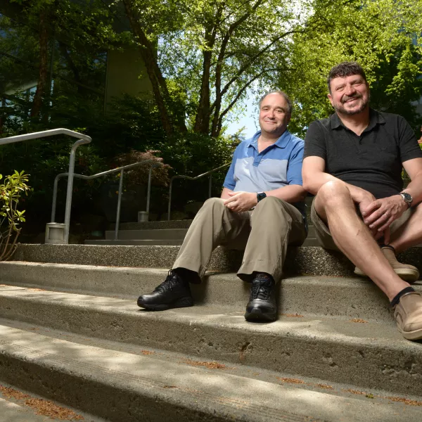 Victor Poznanski and Bernhard Kohlmeier sit together on some steps surrounded by trees and an office building