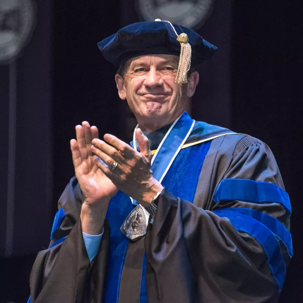 A man wearing academic regalia is smiling and clapping