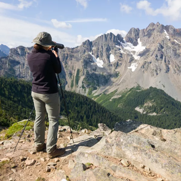 a woman uses a scope to scan the distant, craggy mountainside