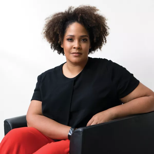 Ijeoma Oluo sits in a modern arm chair, facing the camera 