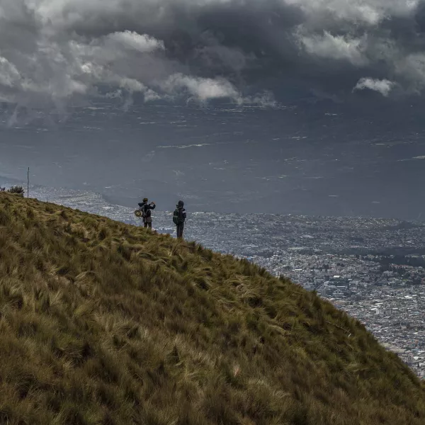 A Western professor and a student standing on a grassy hill overlooking Pichincha on a cloudy day