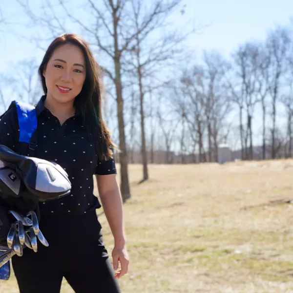 Cathy Kim stands on a golf course, a golf bag and clubs over her shoulder
